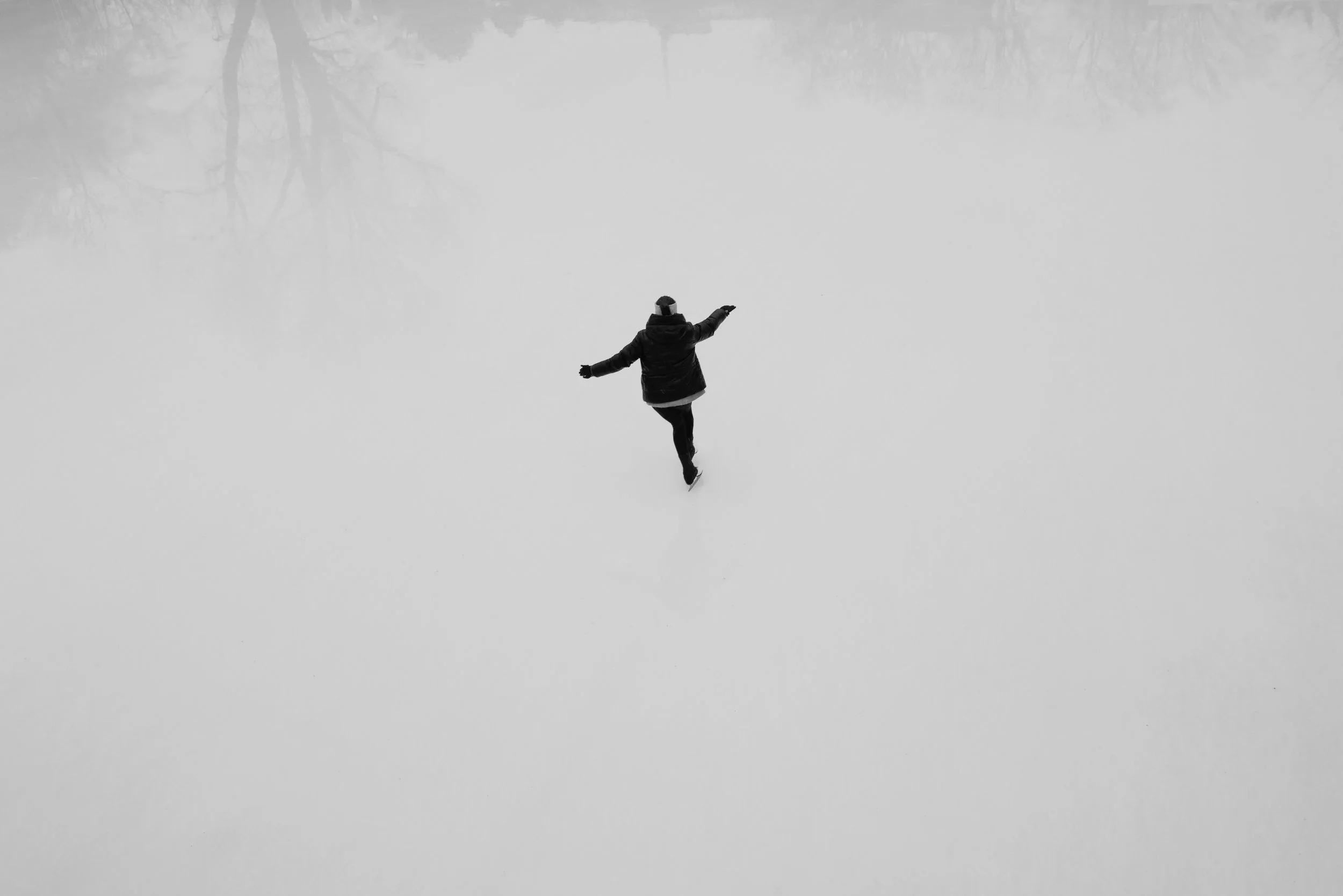 Person läuft auf schneebedecktem Feld mit Armen ausgestreckt, Luftaufnahme.