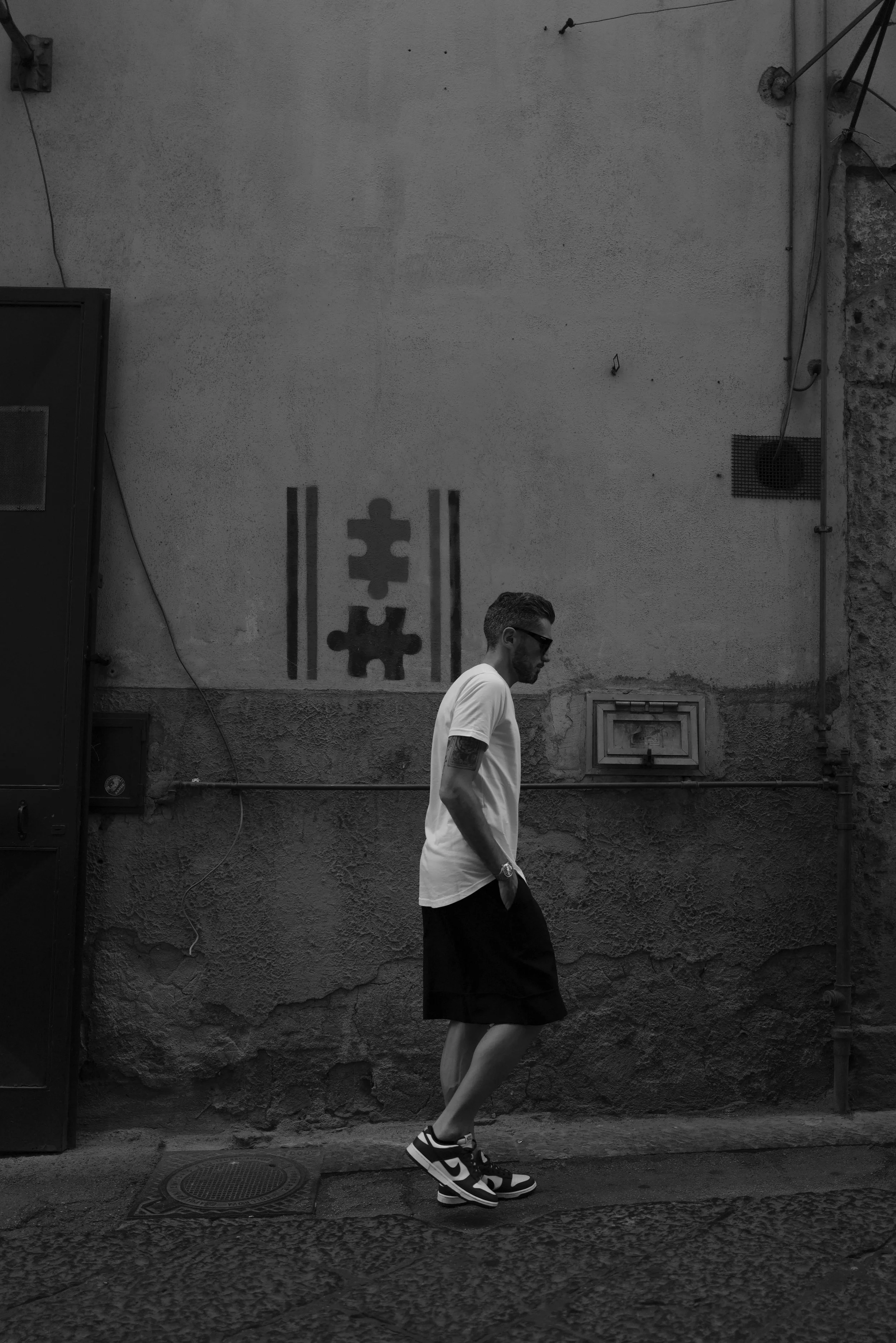Mann in weißem T-Shirt und kurzer Hose geht an einer alten Mauer mit Graffiti-Muster vorbei.