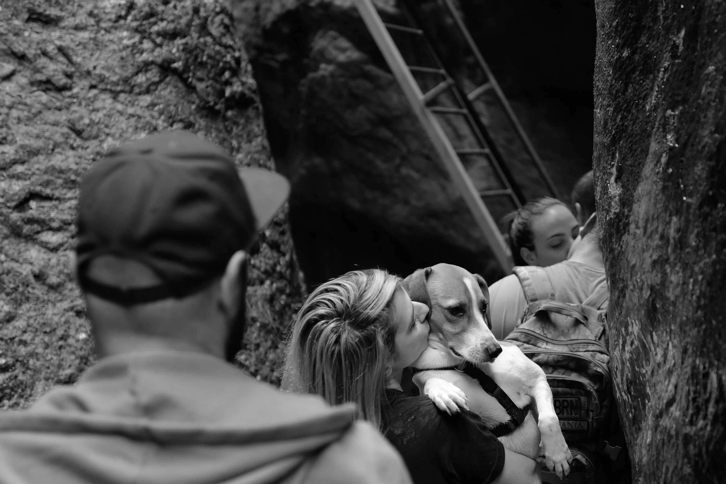 Mehrere Menschen in einer felsigen Schlucht, eine Person hält einen Hund, eine Leiter im Hintergrund.
