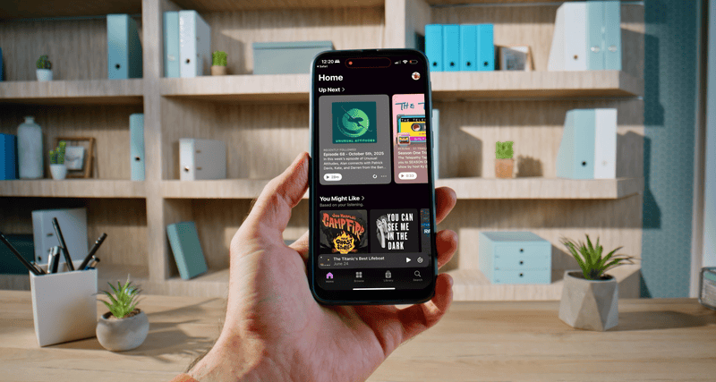 A person holding a smartphone displaying a podcast app, with books and potted plants in the background.