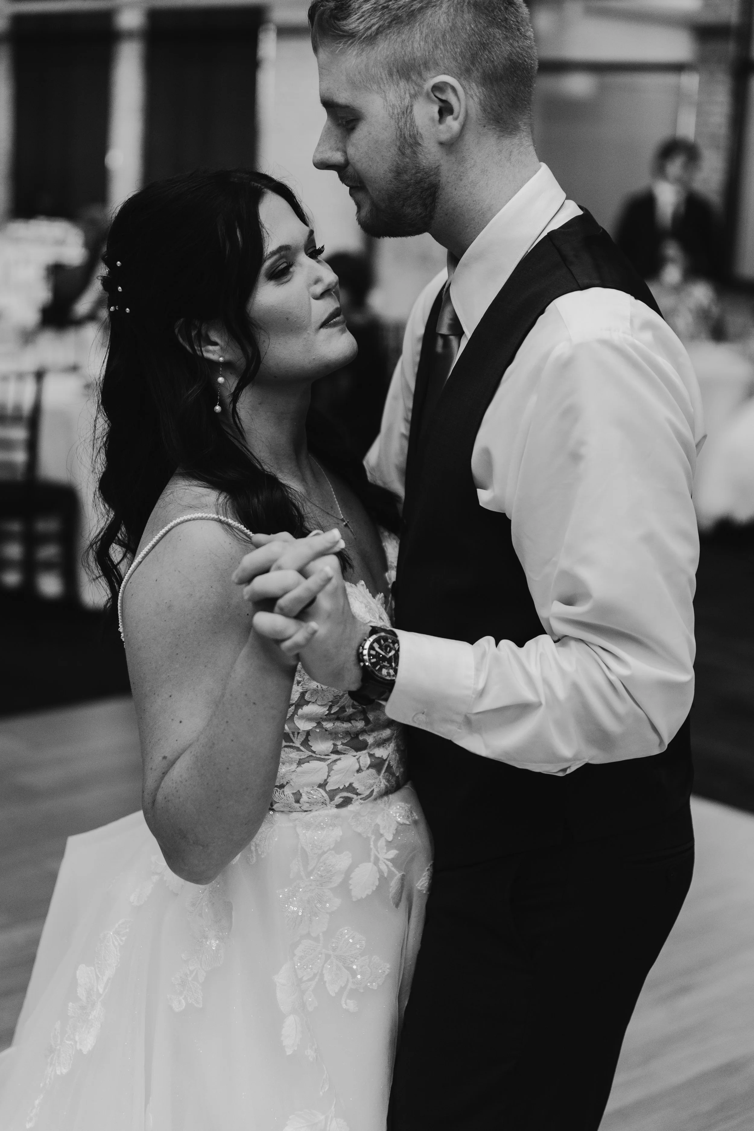 A black and white photo of a bride and groom dancing closely at their wedding reception, holding hands and gazing at each other.
