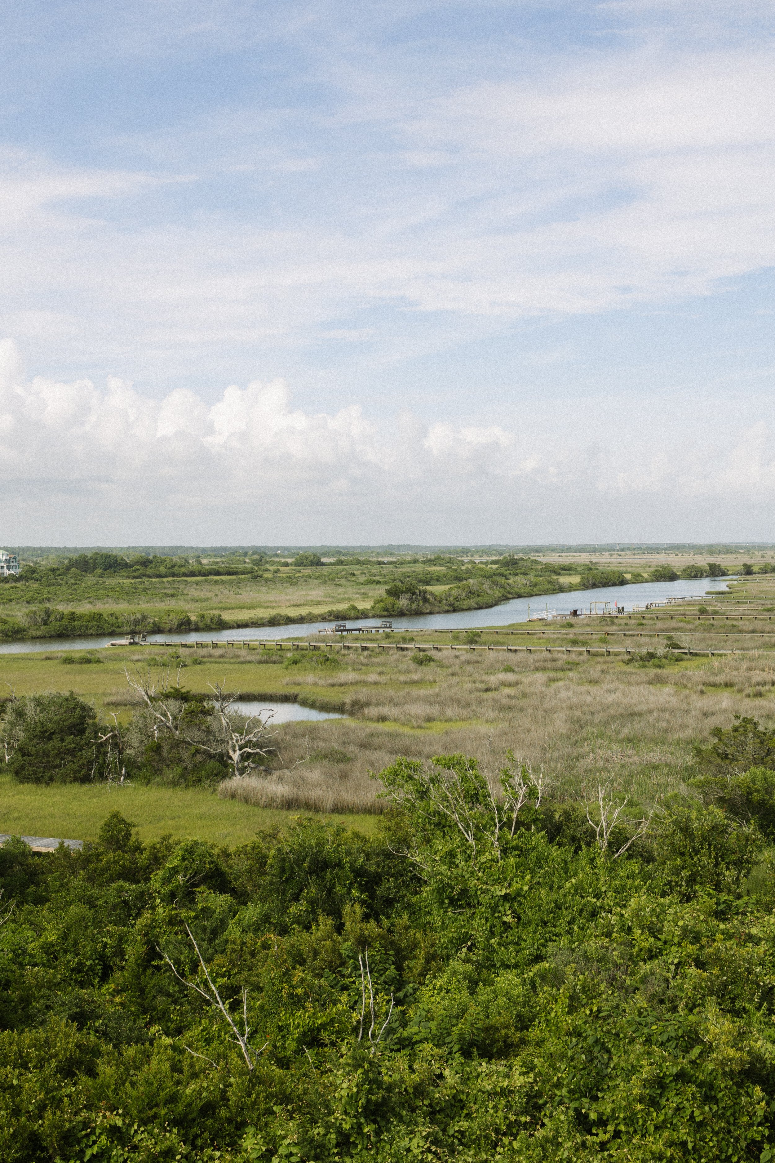 A landscape with a river meandering through lush green vegetation under a partly cloudy sky.