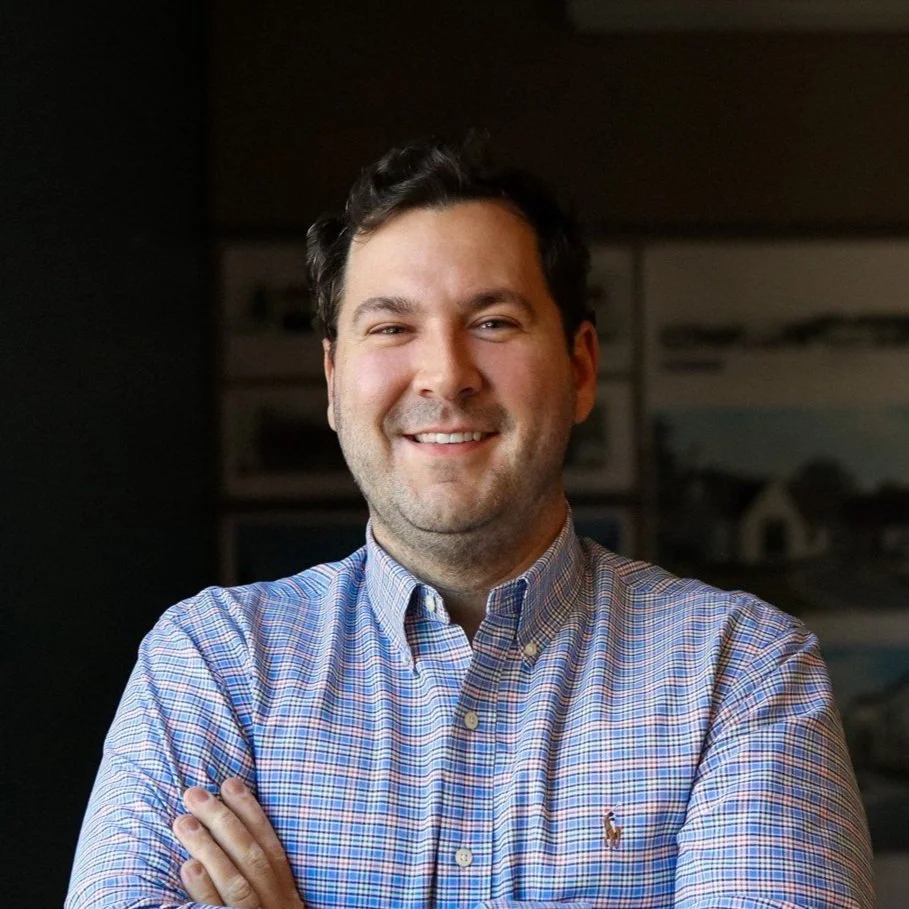Somdal Associates architecture interior design, louisiana, shreveport, baton rouge, A smiling man with dark hair wearing a blue plaid shirt with arms crossed, standing indoors.