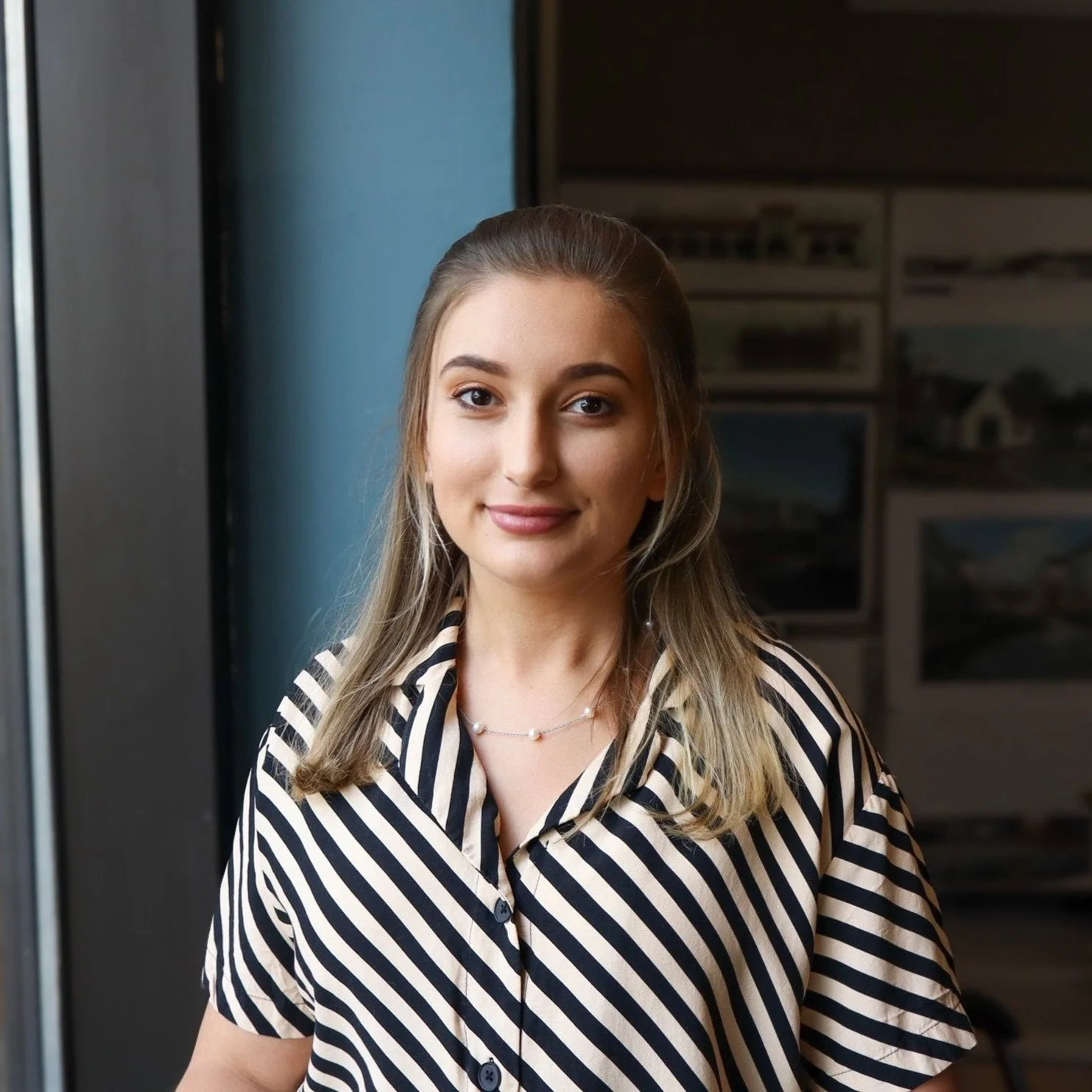 Somdal Associates architecture interior design, louisiana, shreveport, baton rouge, A young woman with light brown hair and a striped black and white shirt standing indoors in front of a wall with framed pictures.