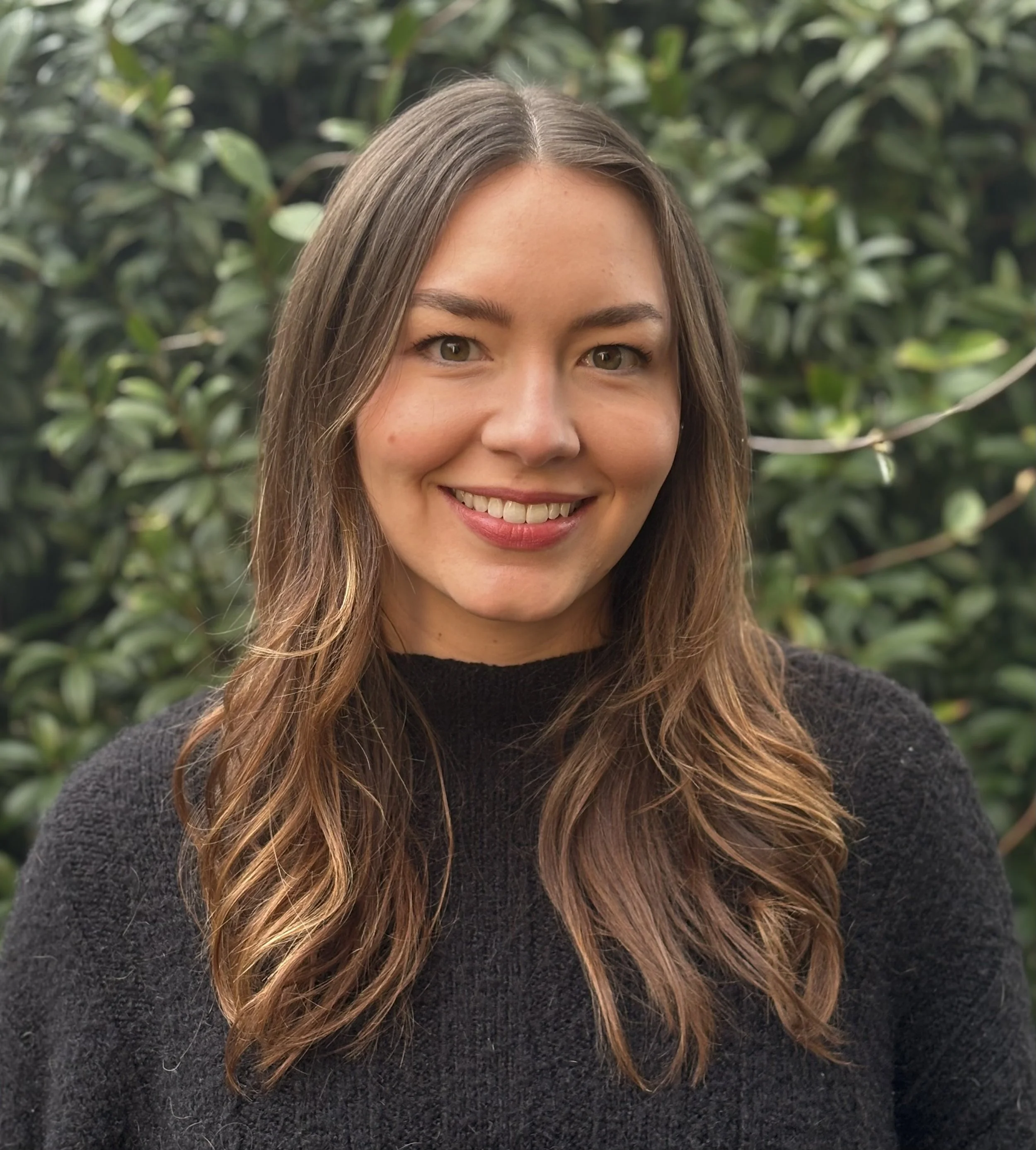 Woman with long blonde hair smiling in front of red foliage