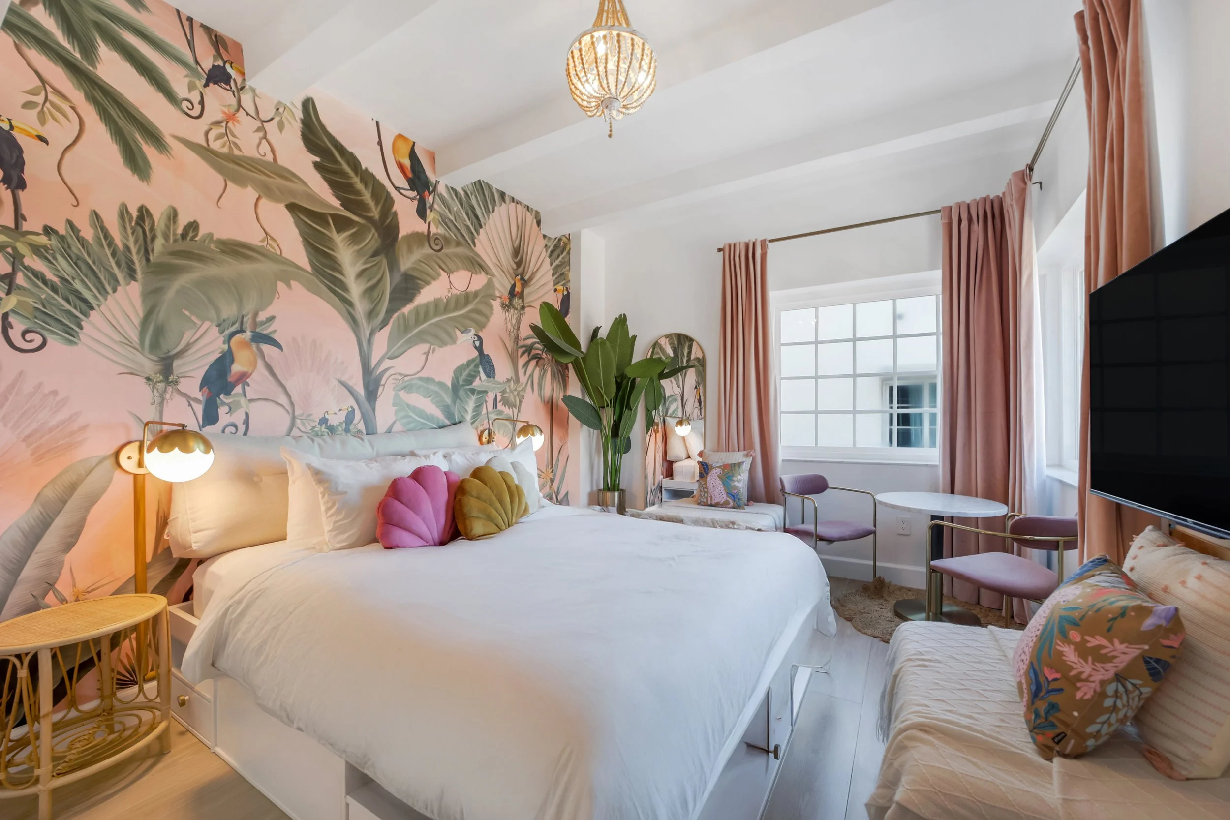 Boutique hotel room at Le Particulier Miami featuring a tropical mural with toucans and palm leaves, pastel pink curtains, plush bedding, and stylish decor, blending Art Deco inspiration with modern Miami Beach elegance.