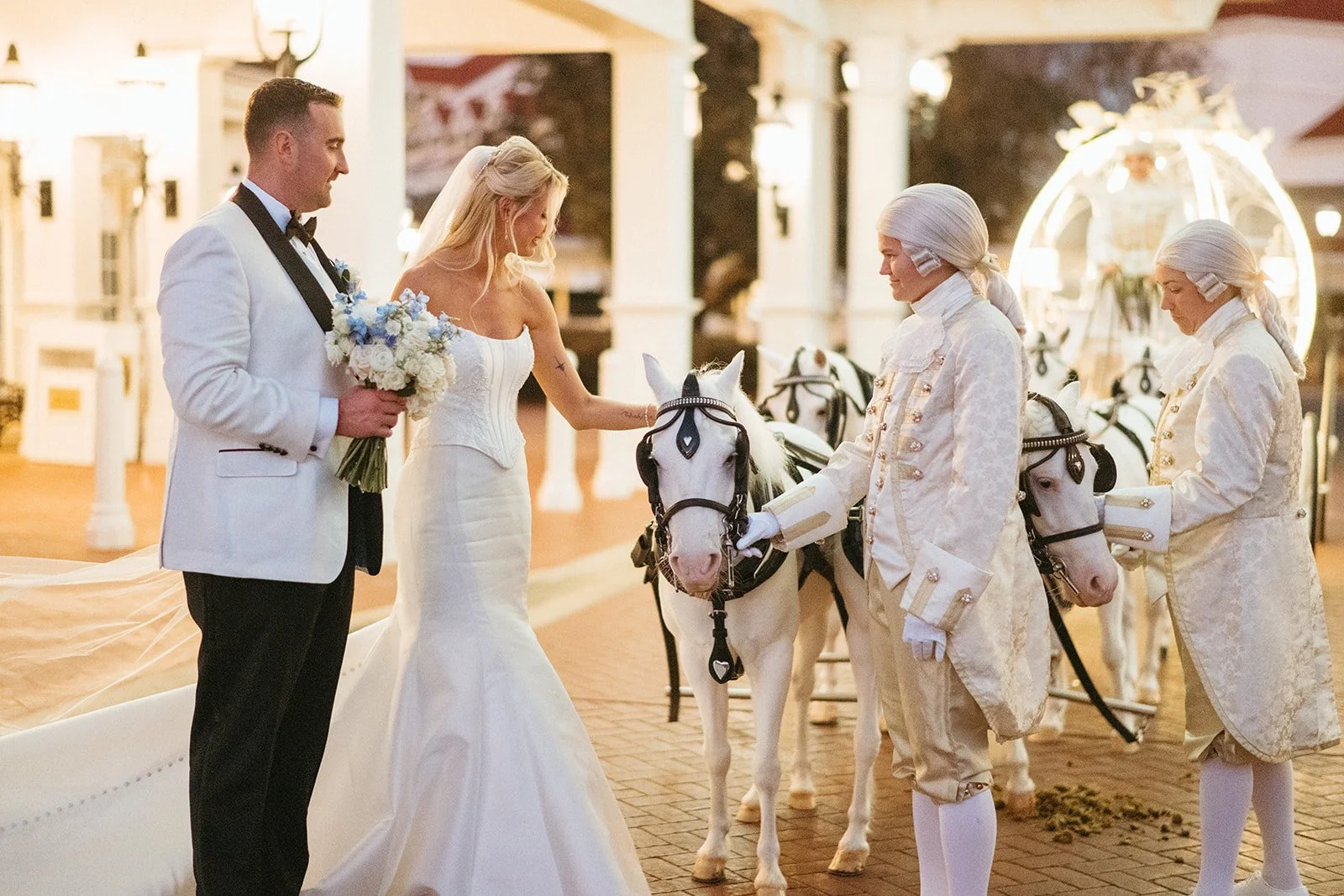 A bride and groom in wedding attire petting a horse at an outdoor wedding ceremony, with groom's parents dressed in historic costume-style outfits.