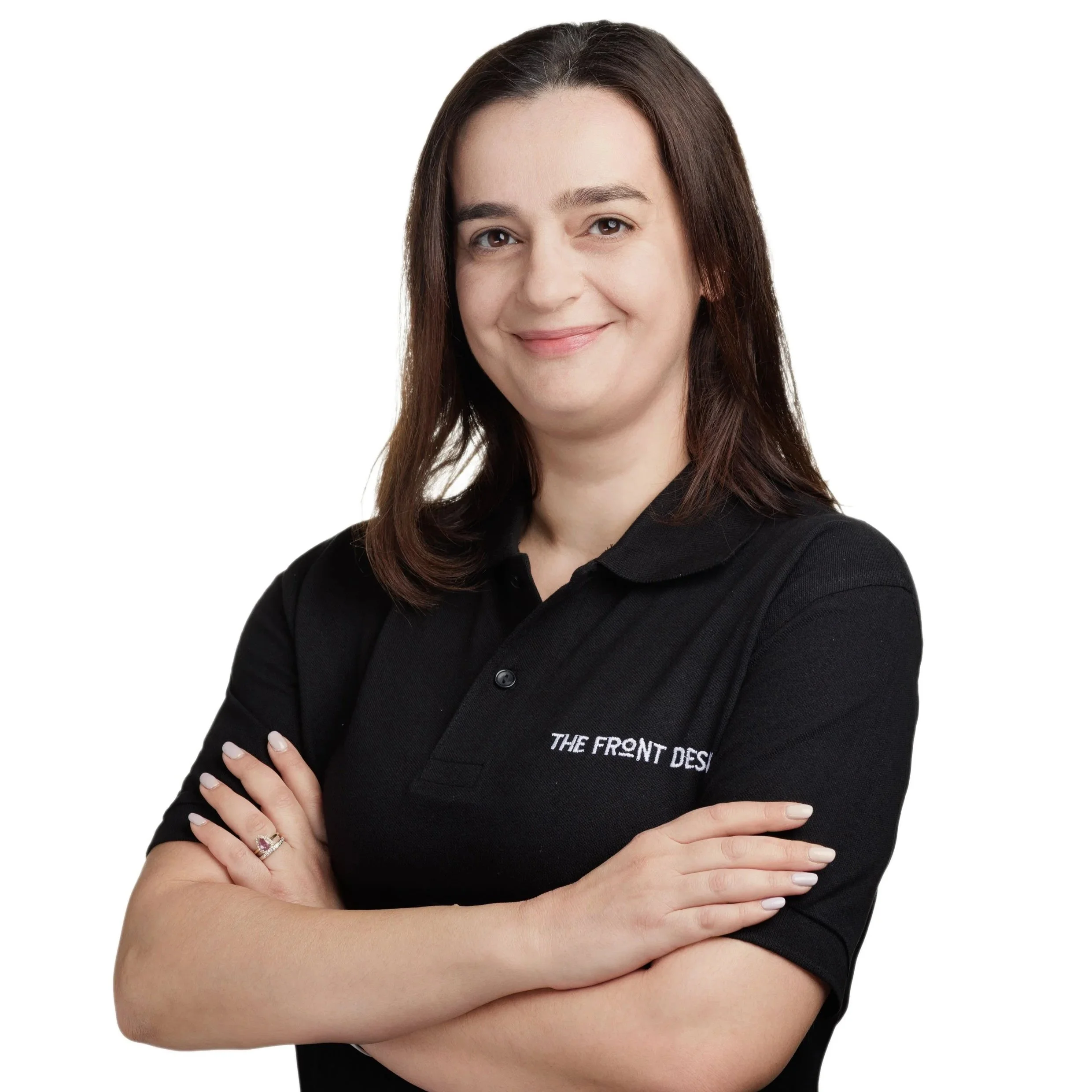 A woman with brown hair, smiling, wearing a black polo shirt with text on it, standing with arms crossed against a white background.