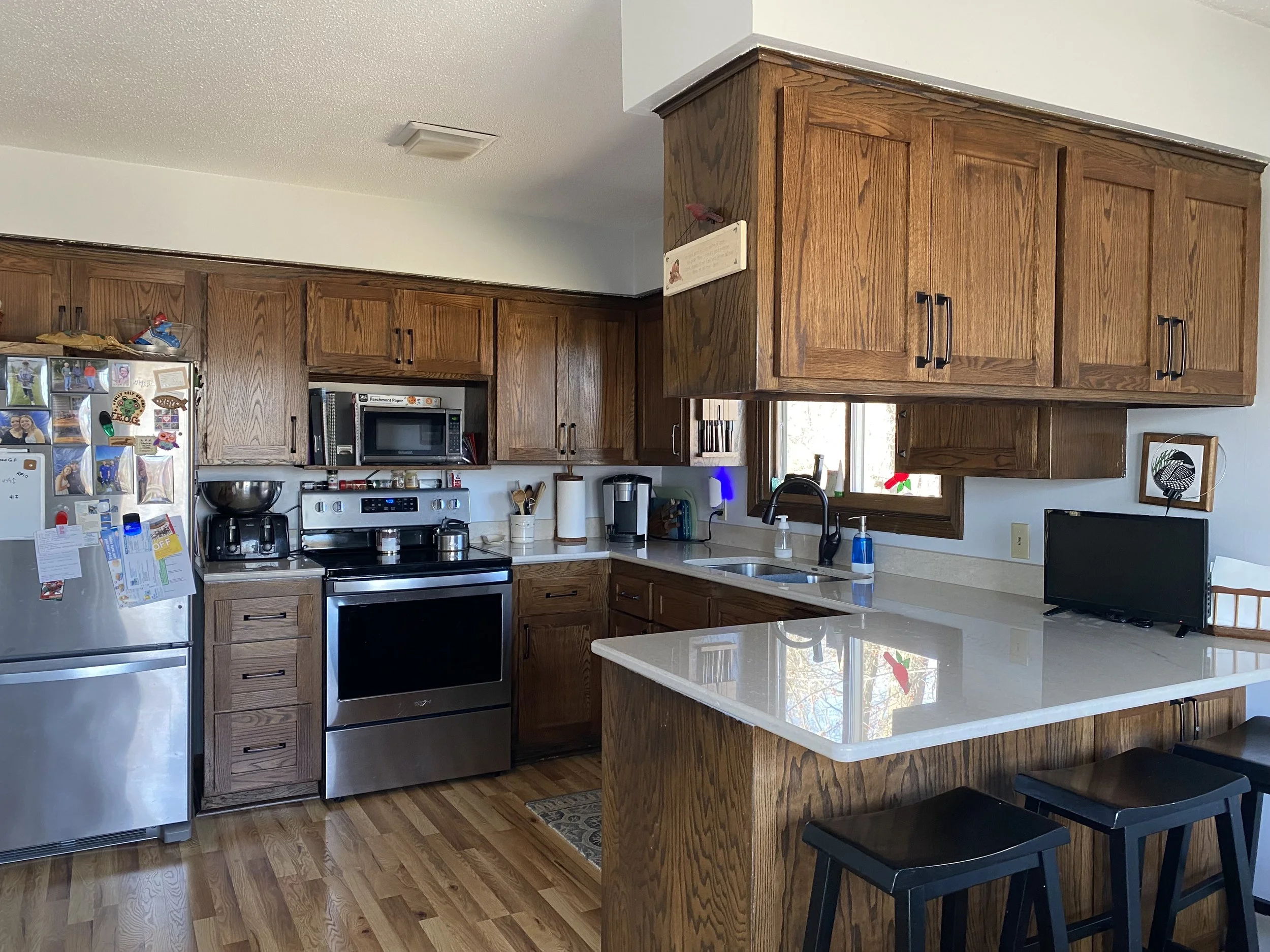 Kitchen with wooden cabinets, stainless steel appliances, a small black television, and a white countertop with a sink.