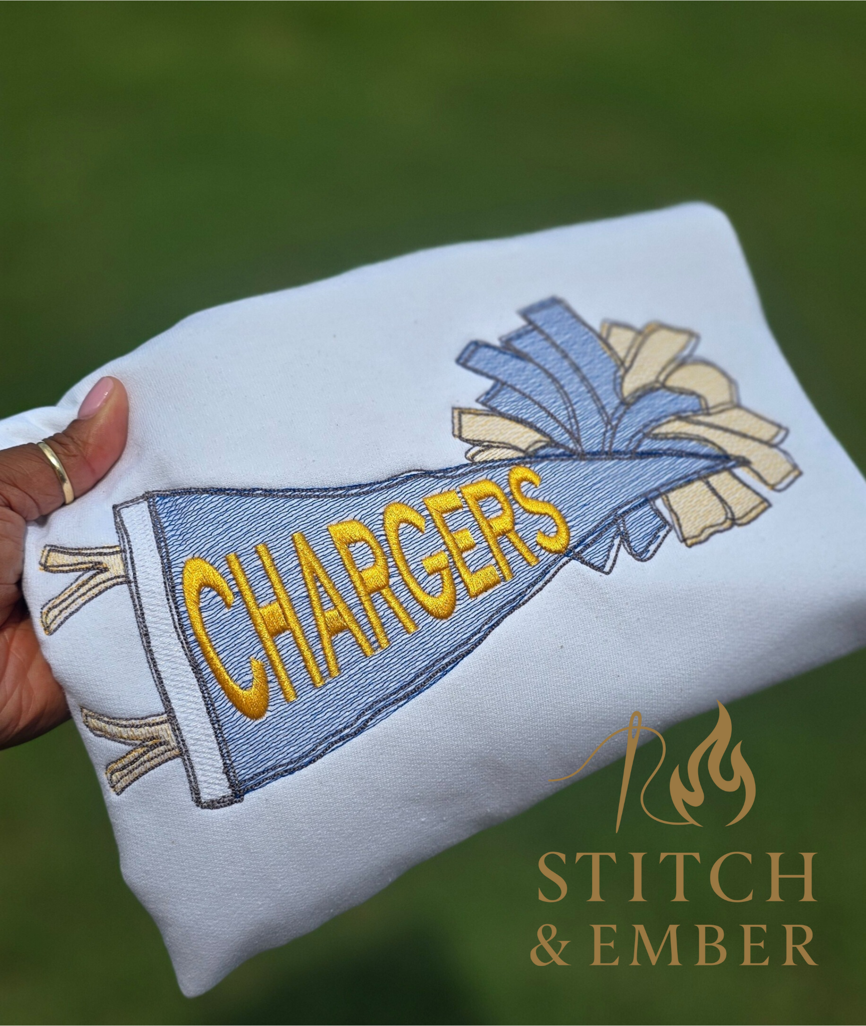 Folded white sweatshirt with embroidered cheerleading megaphone and the word 'Chargers' in yellow