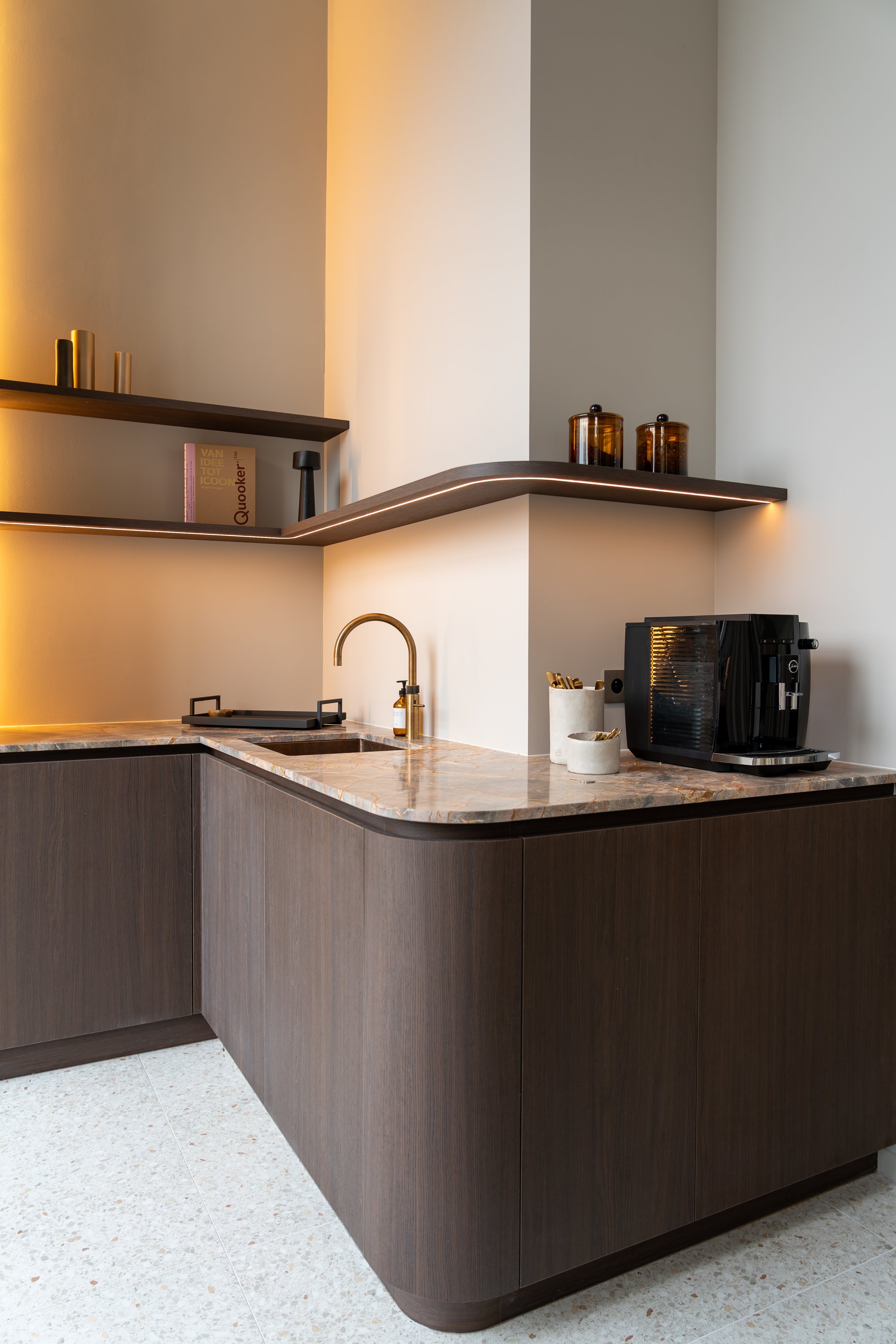 Moderne keuken met donkere houten kasten en marmeren werkblad, inklapbare planken met decoratieve items, een kraan, en een espressomachine. Verlichting zorgt voor een warme sfeer.