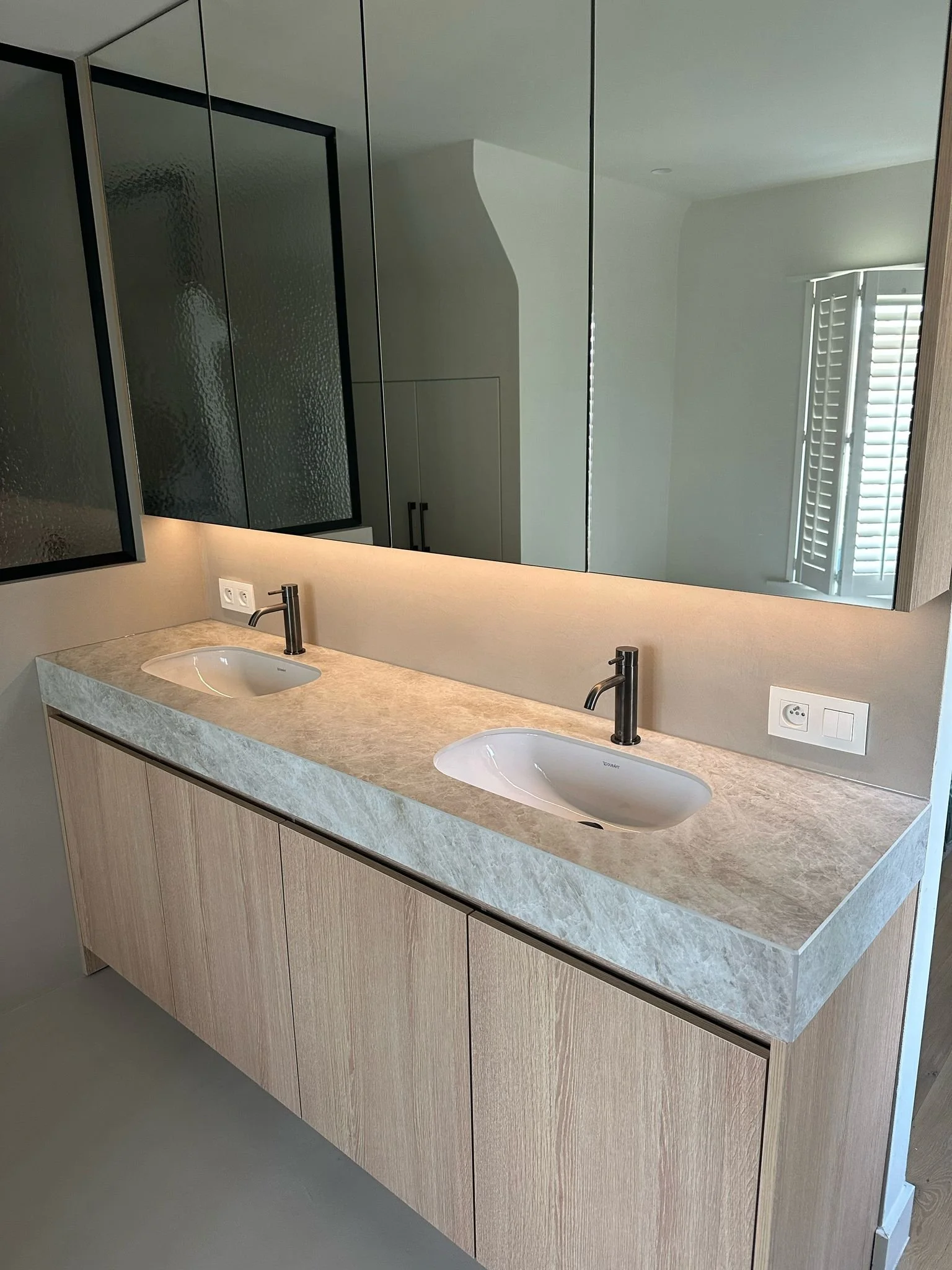 Badkamer met dubbele wastafel, houten kast en moderne designkranen.