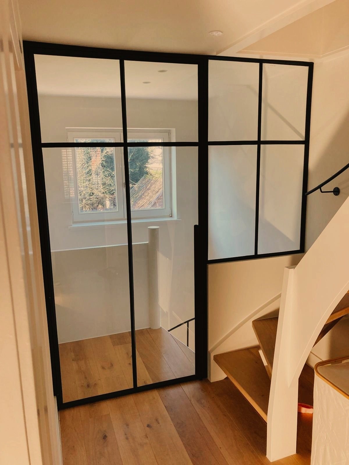Glazen tussenwand met zwarte metalen omlijsting en houten trap.