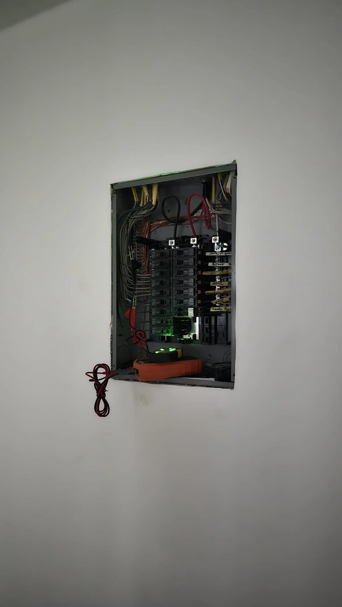 Inside view of an electrical breaker box with multiple wires and circuit breakers, mounted in a wall.