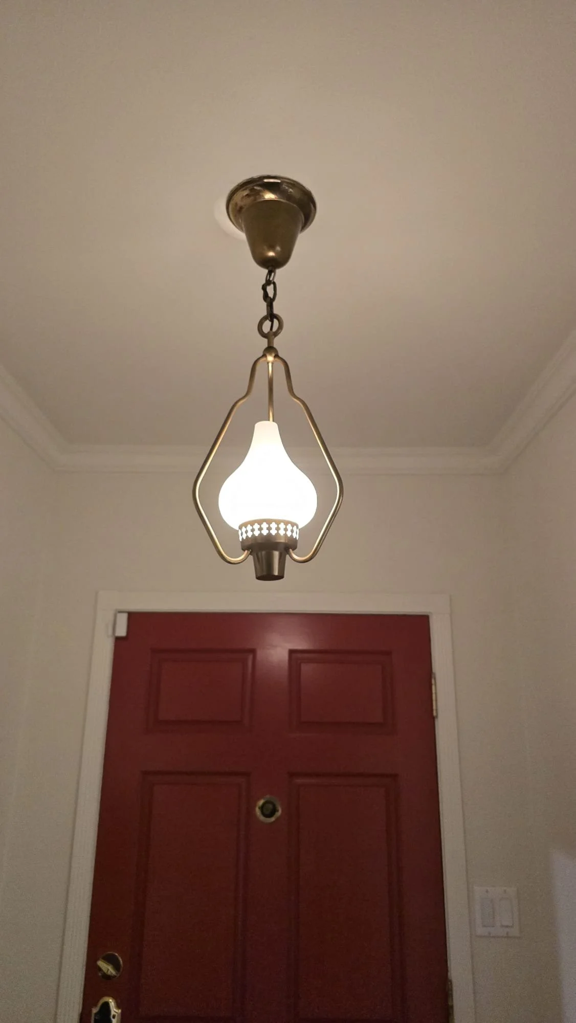 A ceiling light fixture hanging above a red front door with a peephole.
