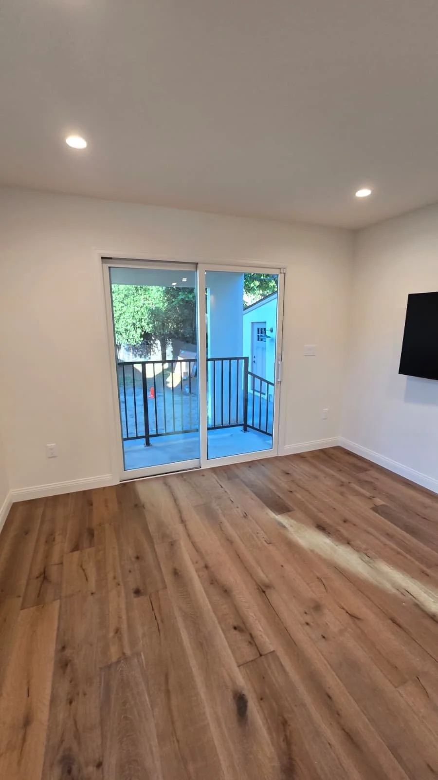 Empty room with hardwood flooring, sliding glass door leading to a balcony, and a wall-mounted TV.