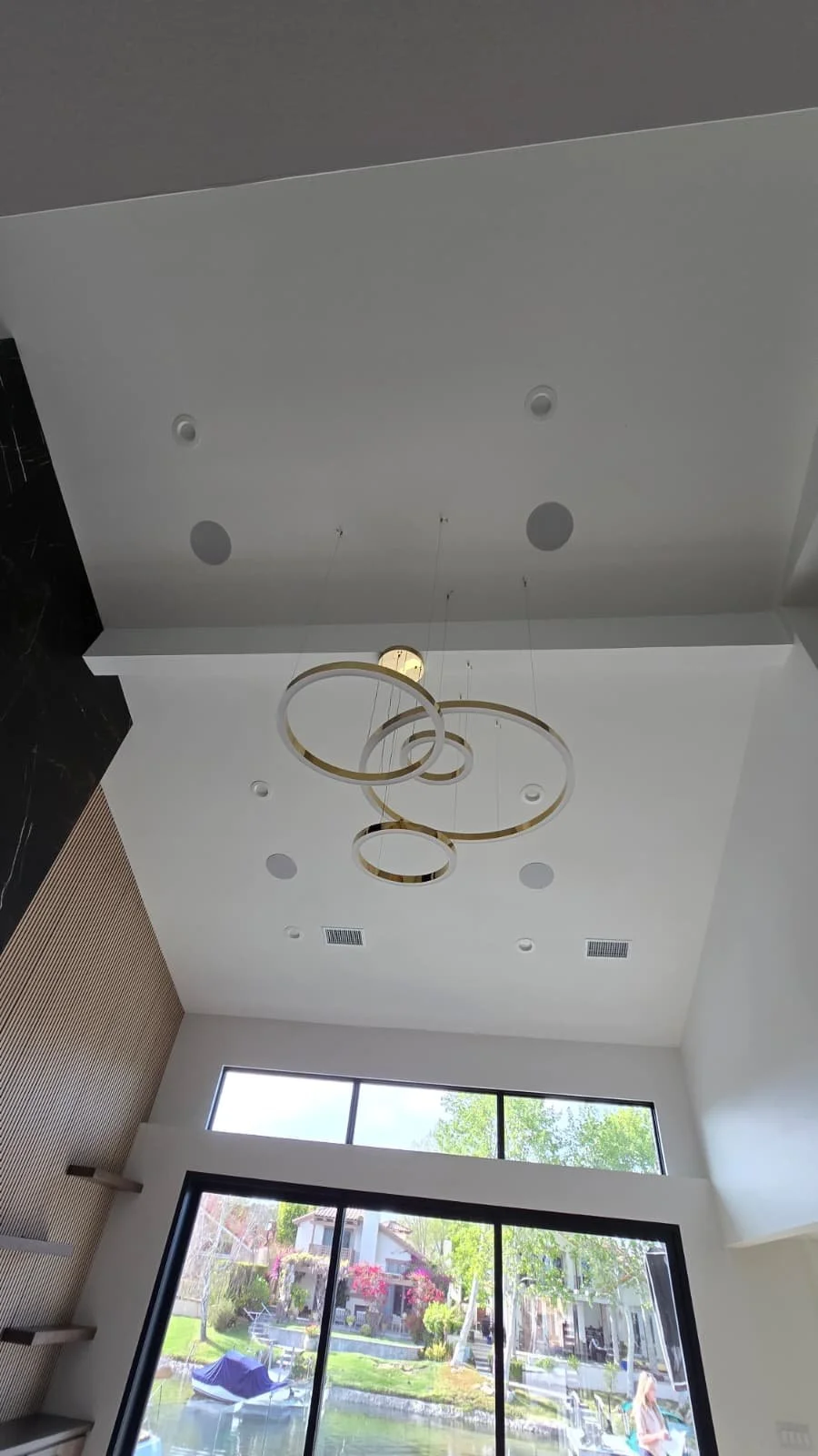 Modern living room with large floor-to-ceiling window, interior ceiling light fixture, and built-in wall shelves.