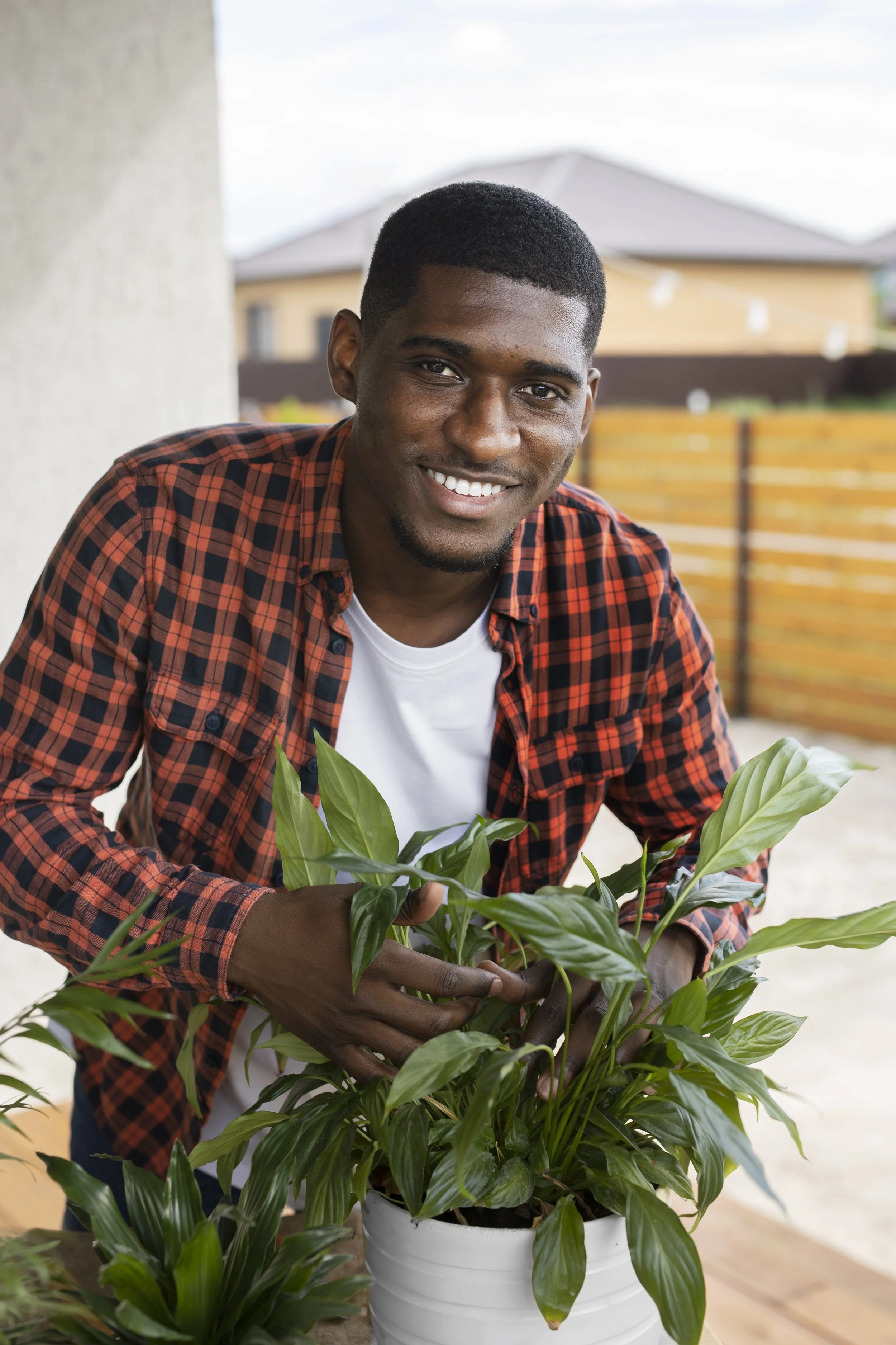Man in plaid shirt smiling while tending to potted plants on a patio.