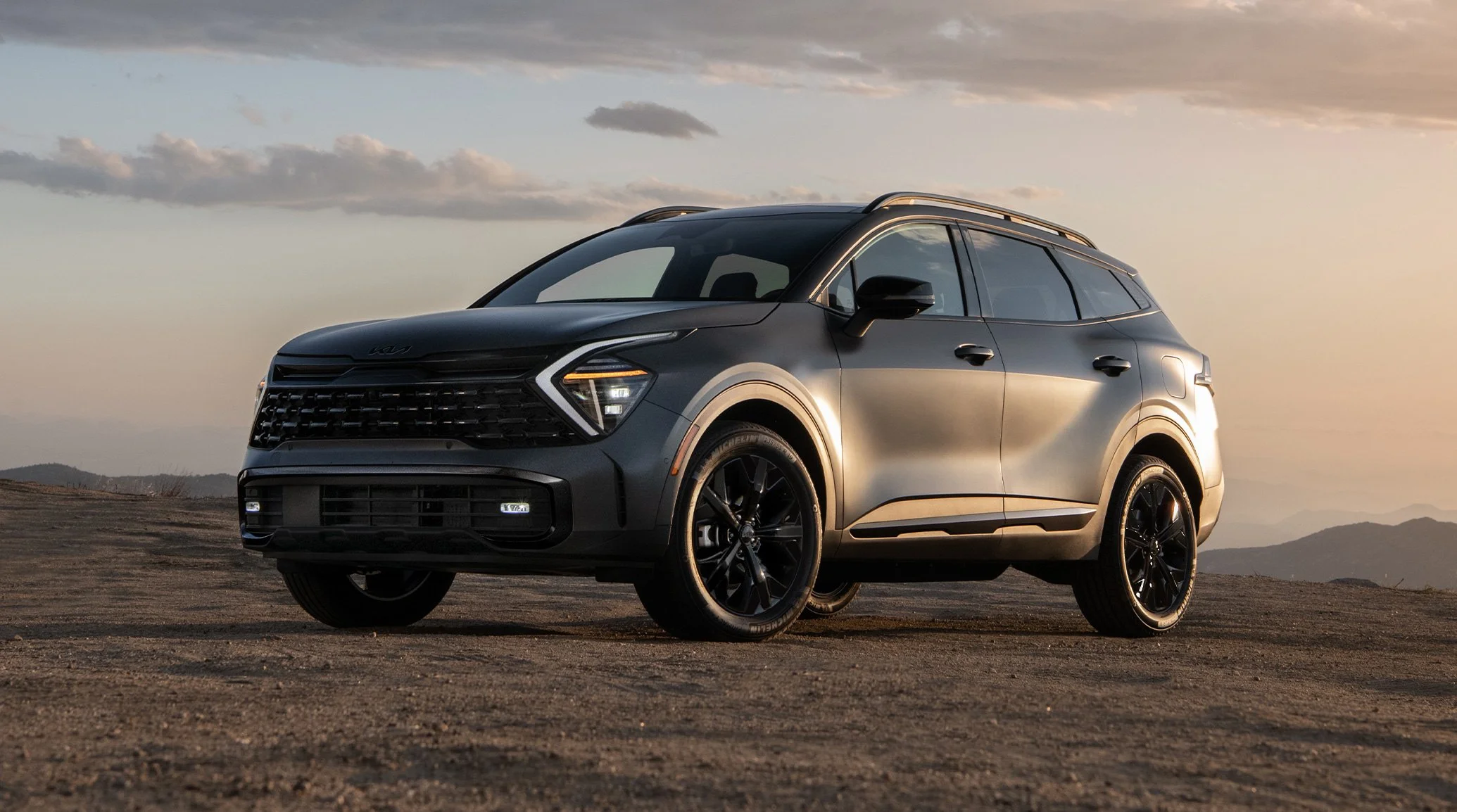 SUV parked on a dirt road at sunset with mountains in the background.