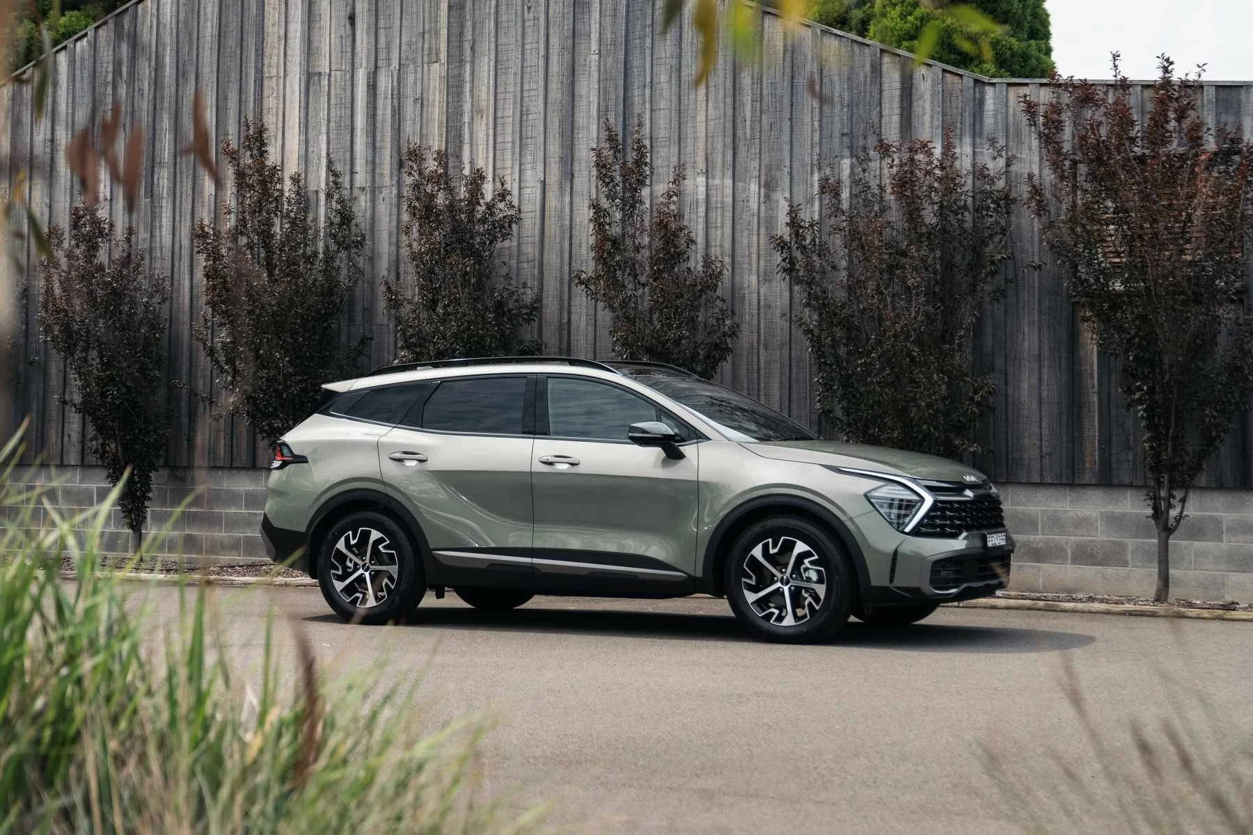 A silver SUV parked on a road in front of a wooden fence and trees.