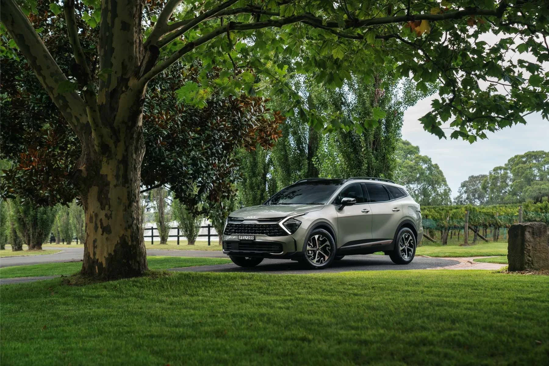 SUV parked on a paved path in a lush green park with trees and grass.