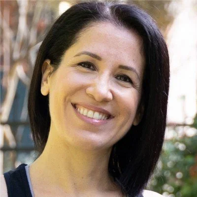 A woman with long dark hair smiling outdoors with trees in the background. Melis Doglu, intuitive eating coach. Iza Clara Healing testimonial. 