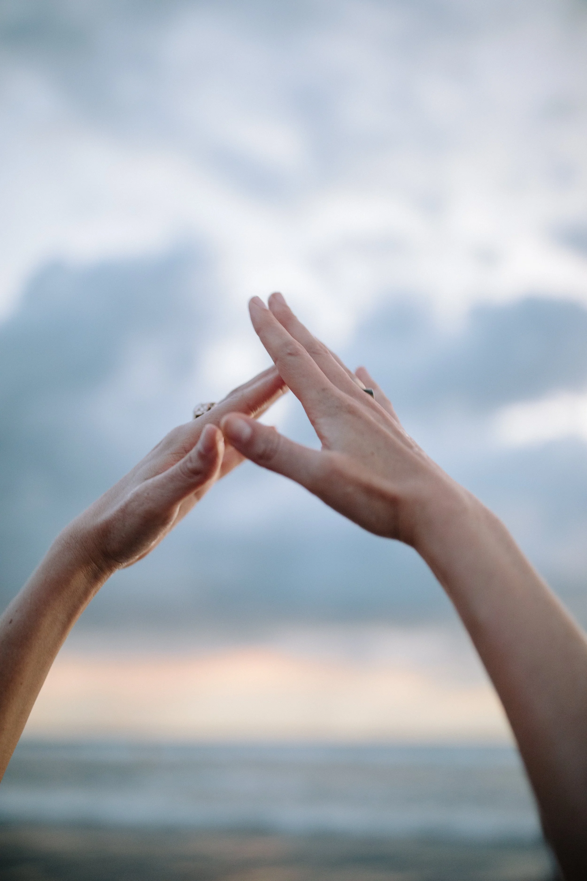 Two hands with rings forming a triangle shape against a cloudy sky background. Iza Clara Healing Offerings. 