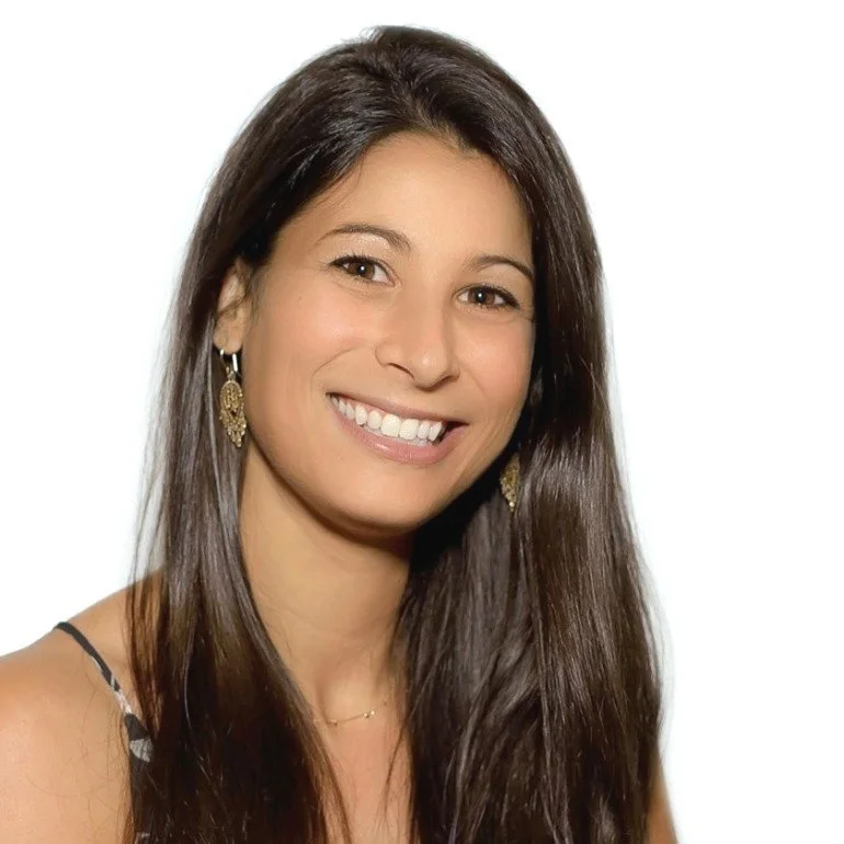 A woman with long dark hair smiling, wearing earrings and a sleeveless top, against a white background. Dalit Barrett, Iza Clara Healing testimonial. 