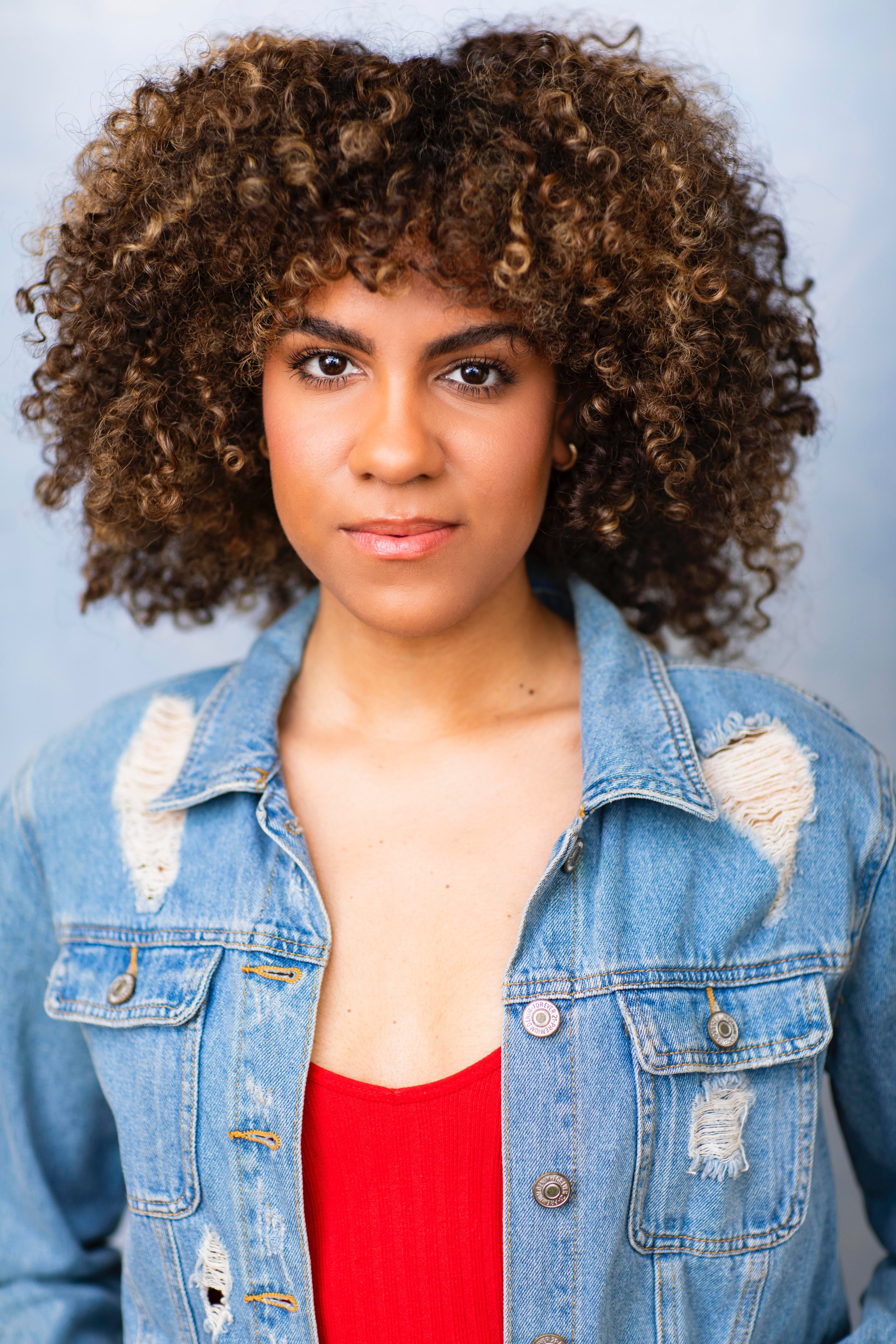 Jolimar looking at the camera wearing a red top and blue, distressed jean jacket