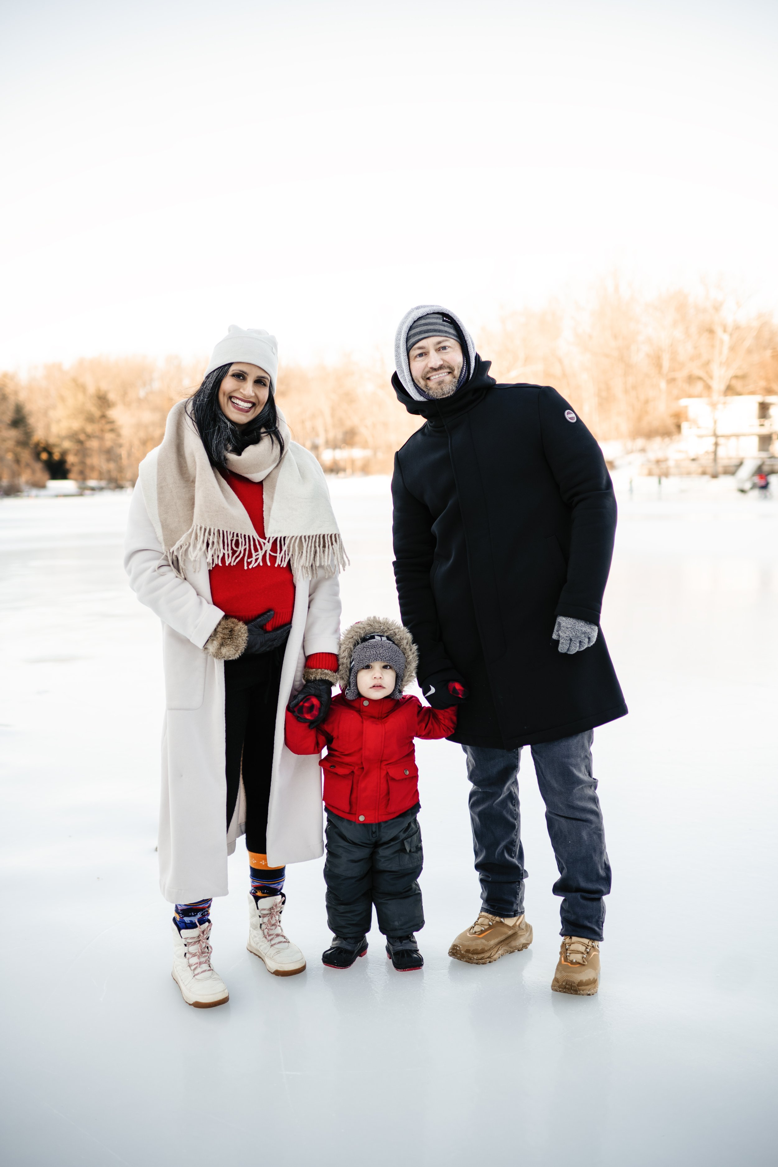 Winter family maternity photography session with parents and children standing on a frozen lake outdoors in the snow.