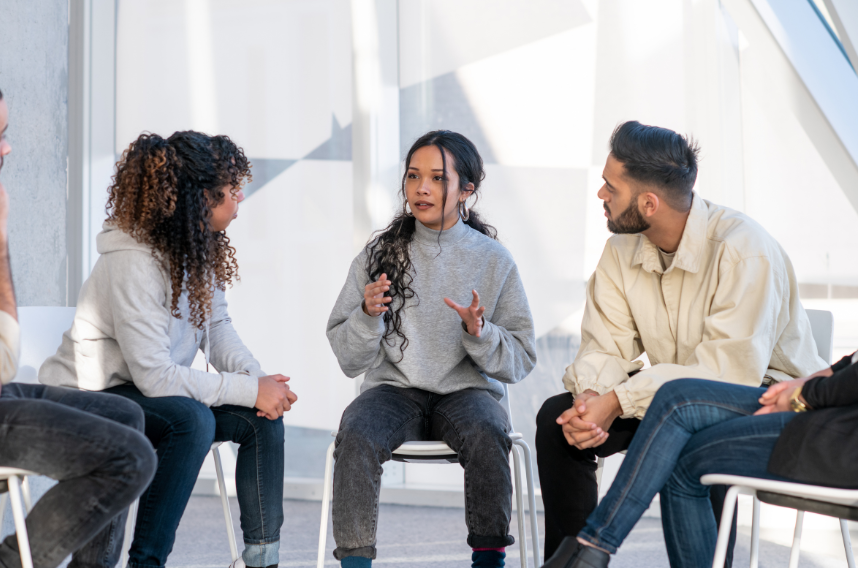 Group of diverse young adults in a circle having a discussion in a modern, well-lit room.
