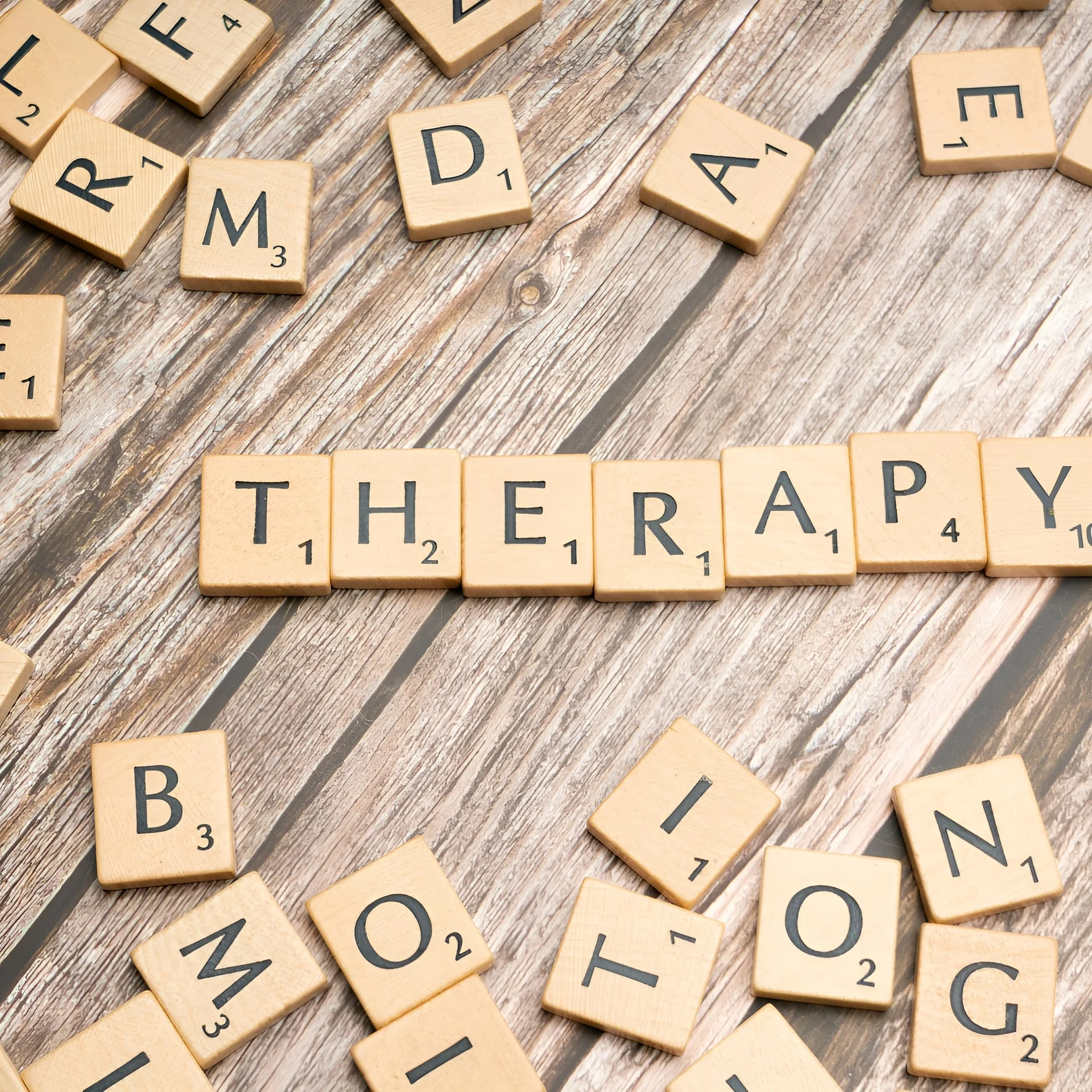 Scrabble tiles spelling 'THERAPY' on a wooden surface.