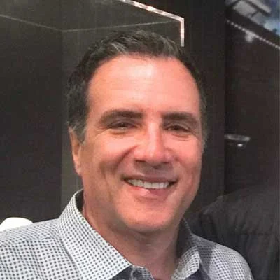 Fred Gaulledi with dark hair and a checkered shirt posing indoors.