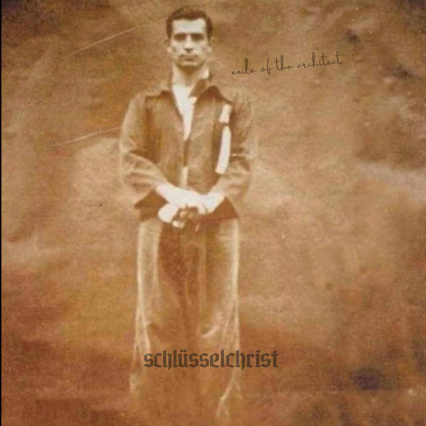 A sepia-toned photograph of a man standing outdoors with trees in the background. He is wearing a dark jacket and light-colored pants, with his hands clasped in front of him, looking directly at the camera.