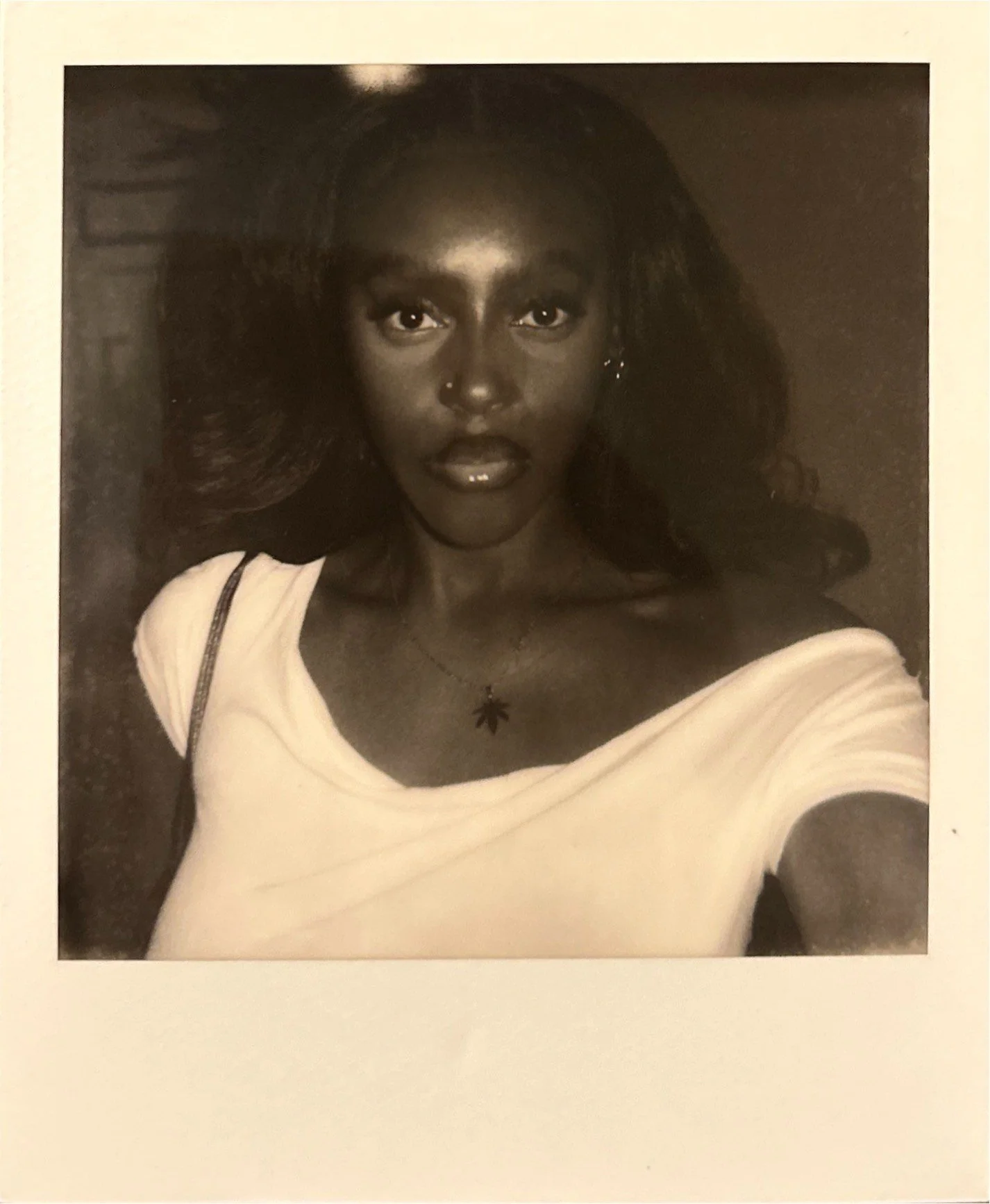 Black and white portrait of a young woman with long hair, wearing a white top, a necklace with a leaf pendant, and earrings.
