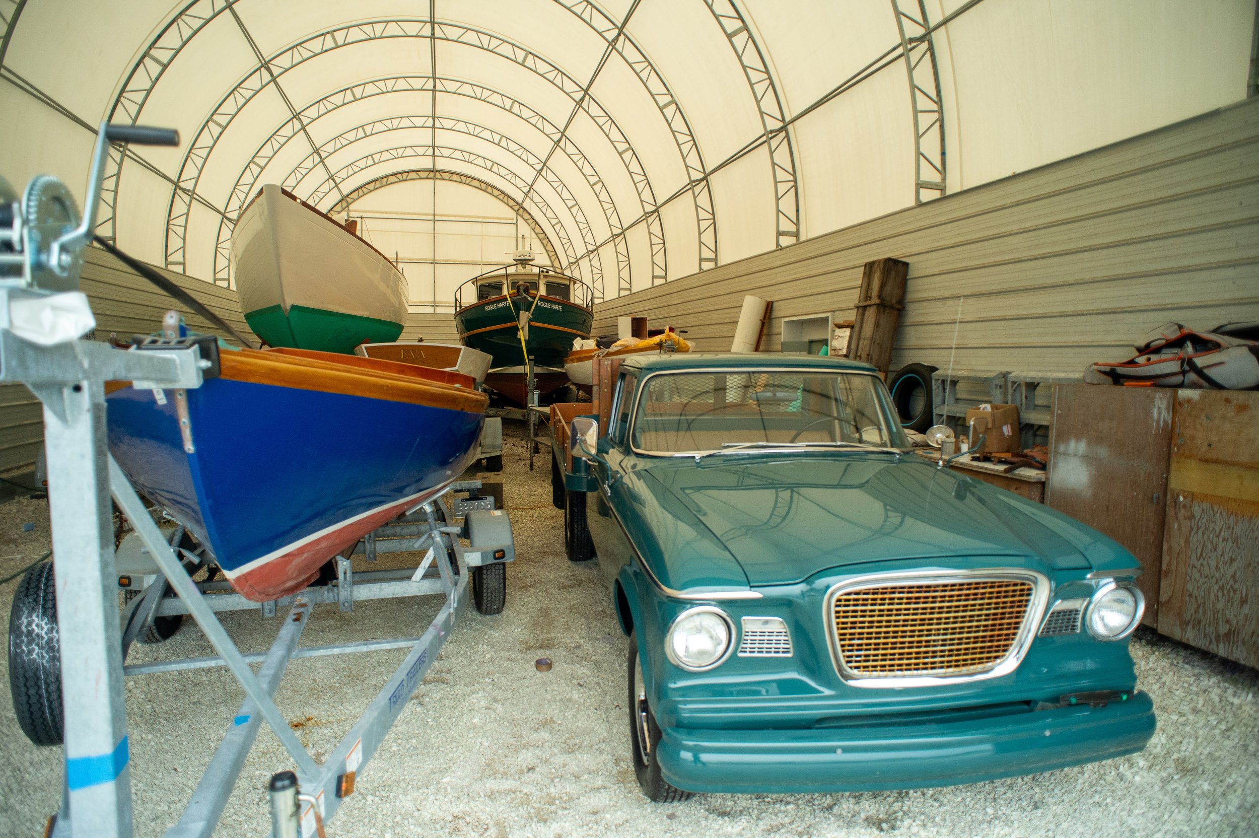 A classic teal car and several boats stored inside a large covered structure.