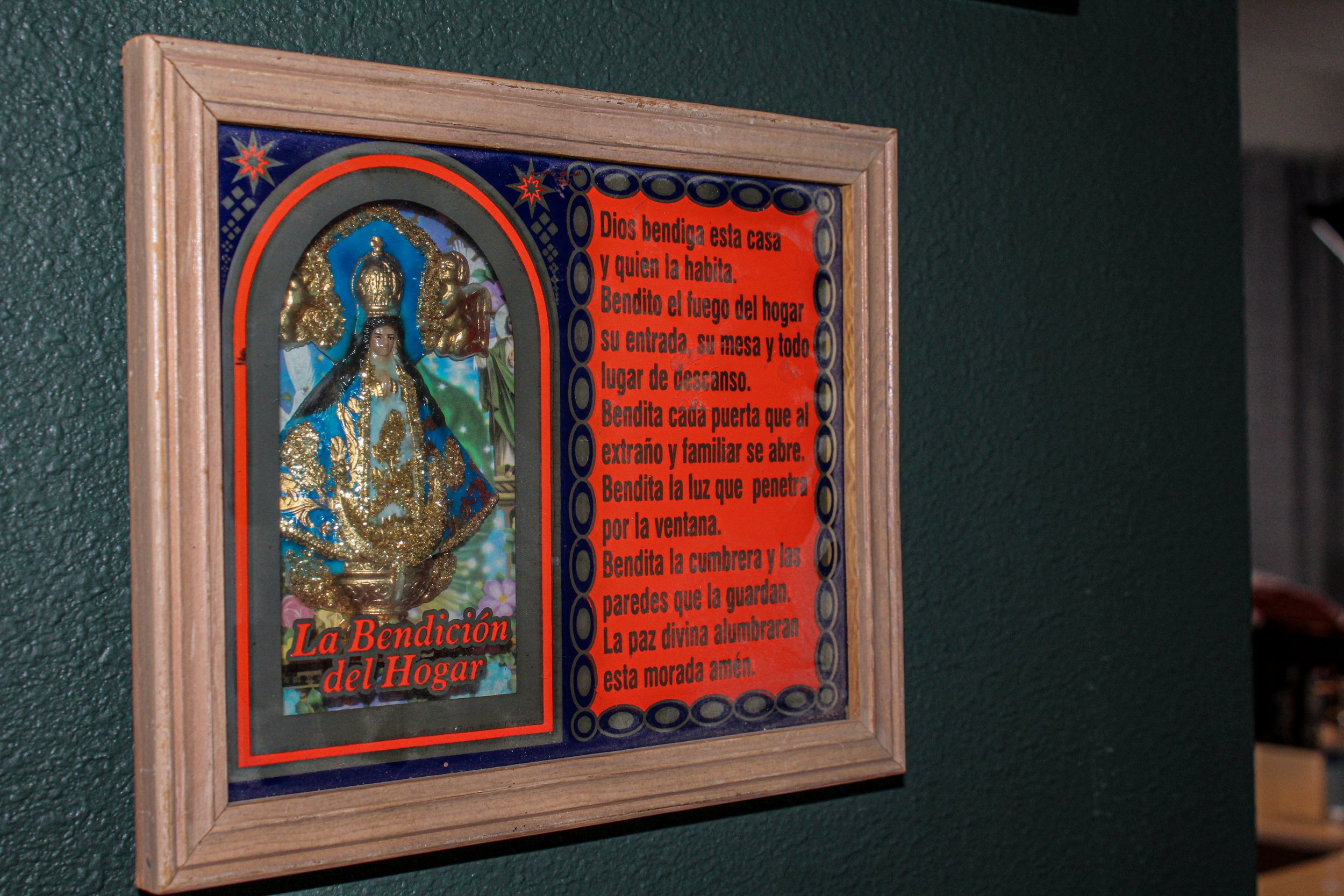 Framed religious image and prayer with Spanish text on a green wall.