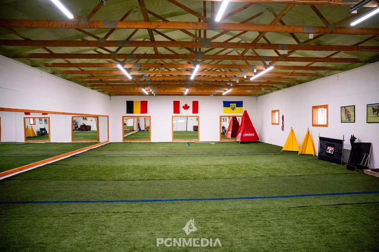 Indoor sports training facility with artificial turf, mirrors on the left wall, flags of Belgium, Canada, and Ukraine on the back wall, various agility and training equipment, and framed pictures of athletes on the right wall.