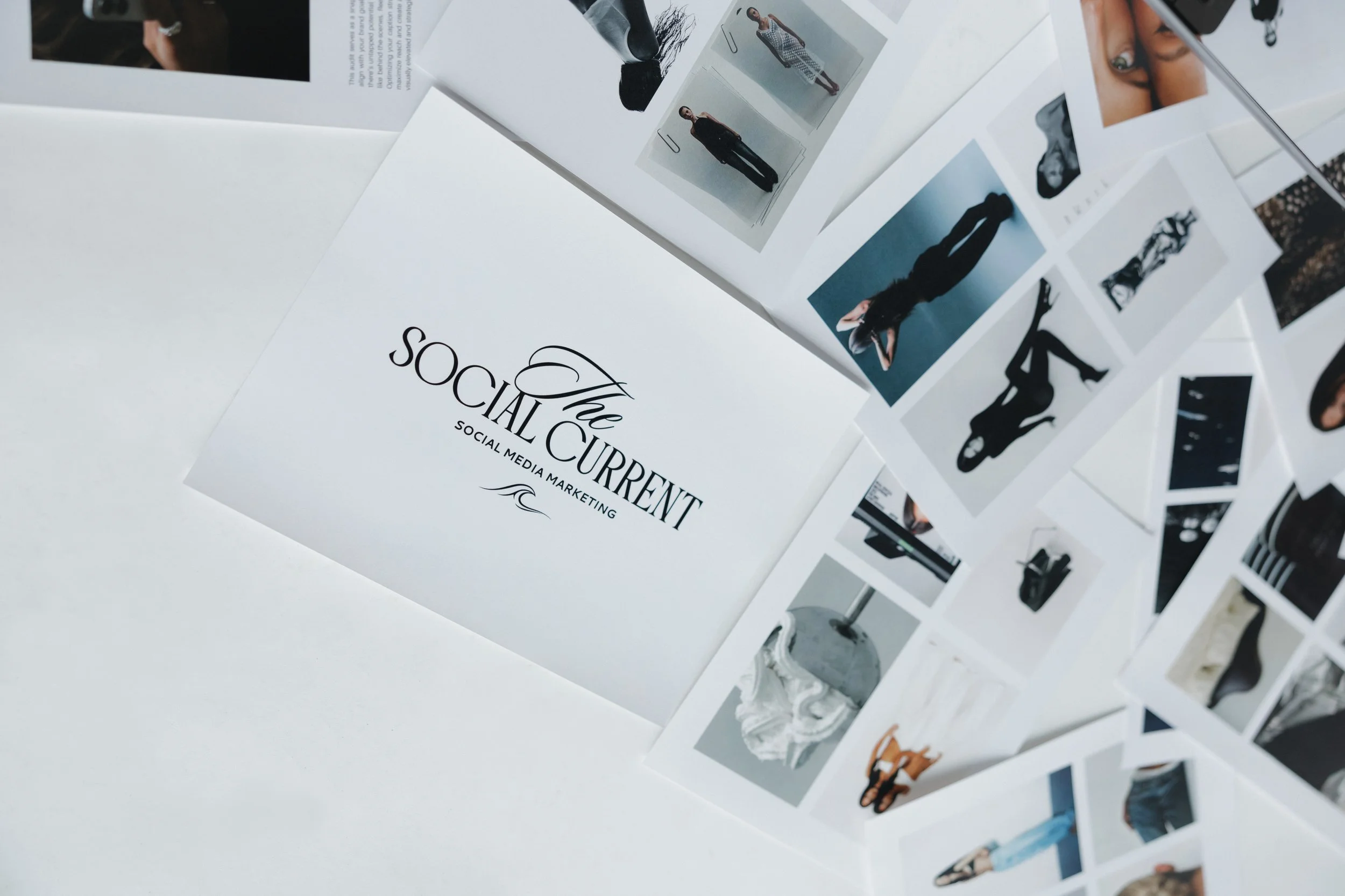 A collection of printed photos and a white sheet with the text "The Social Current" and "Social Media Marketing" on it, arranged on a white surface.