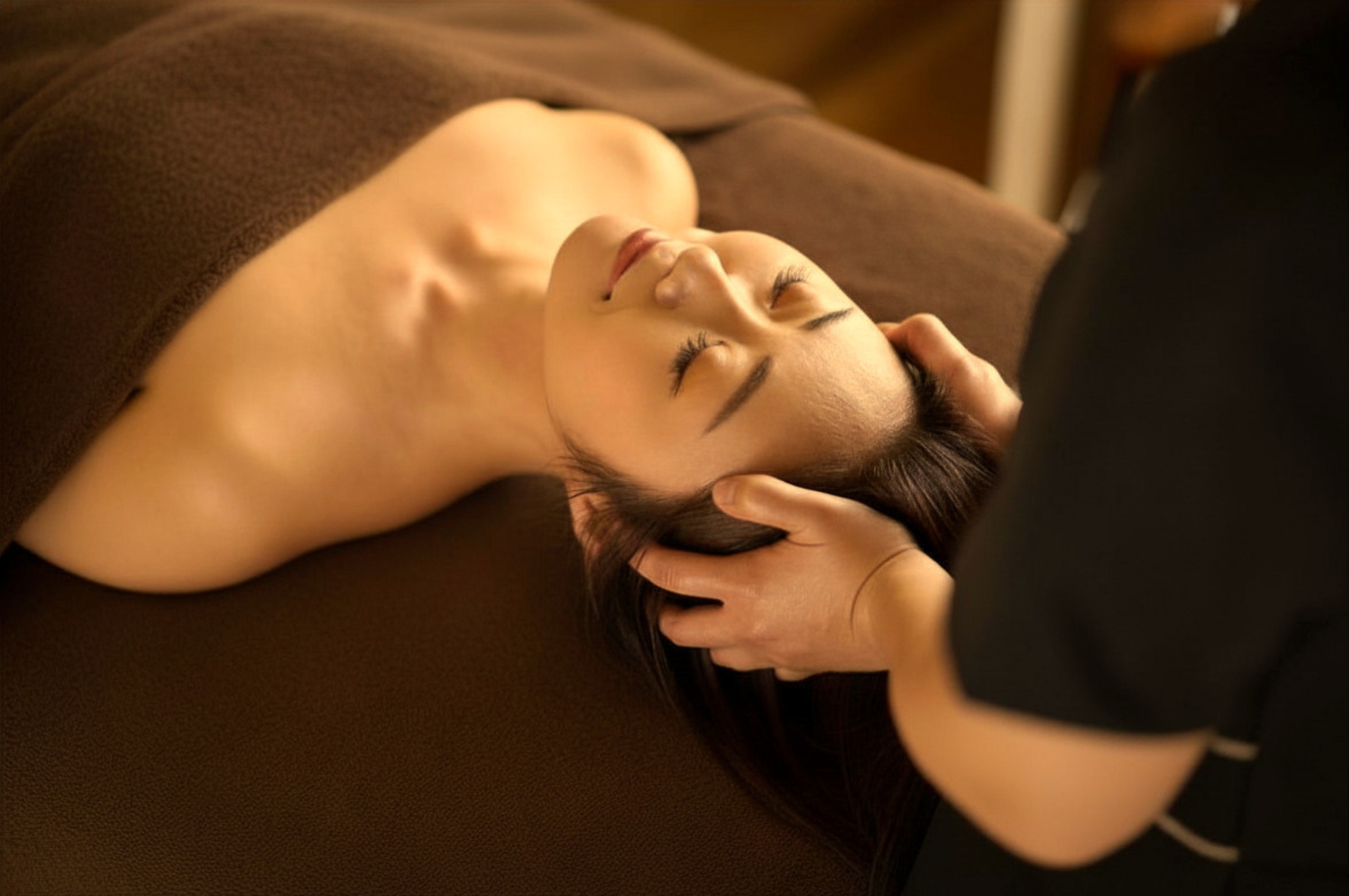 A woman receiving a massage on her head and neck from a massage therapist