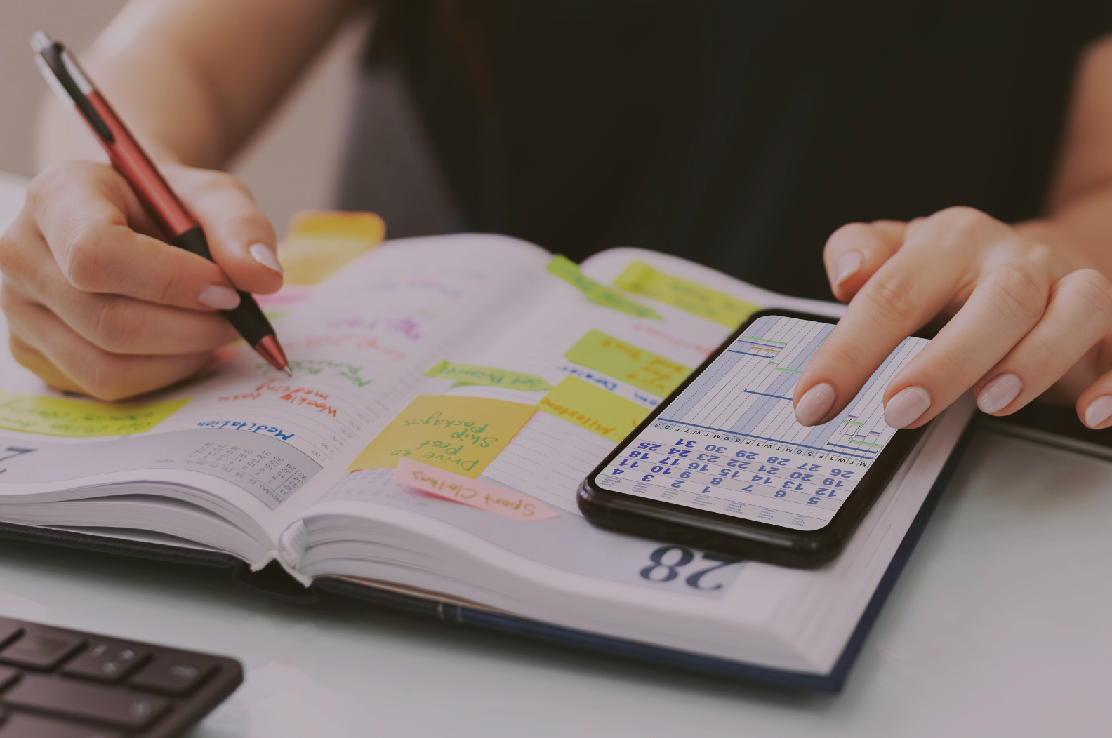 Person organizing planner with sticky notes and managing schedule on smartphone.