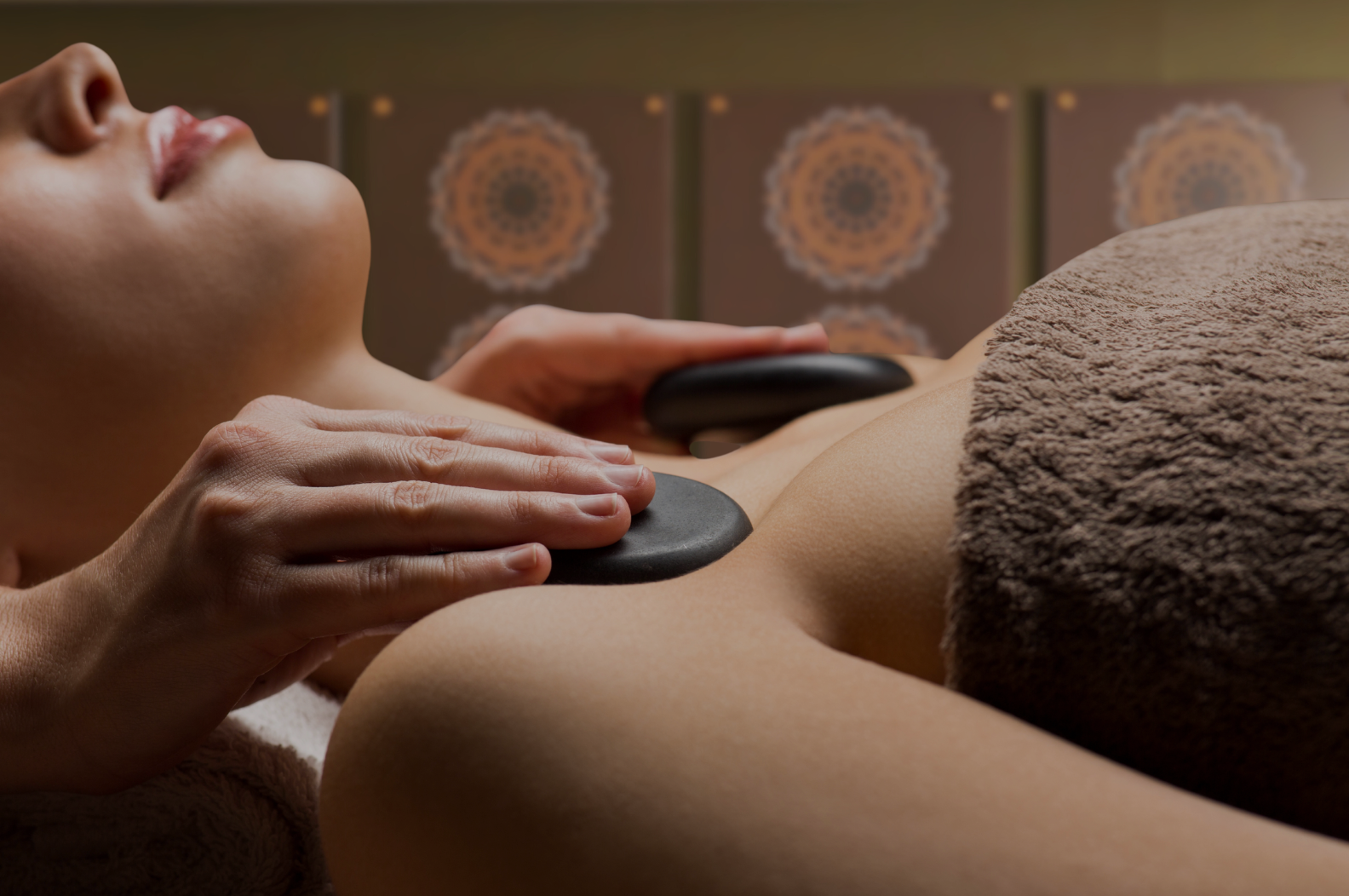 A woman receives a hot stone massage on her back in a spa room with decorative wall art.