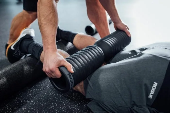 A person receiving body tempering with a practitioner using a heavy steel weight to loosen hamstrings.