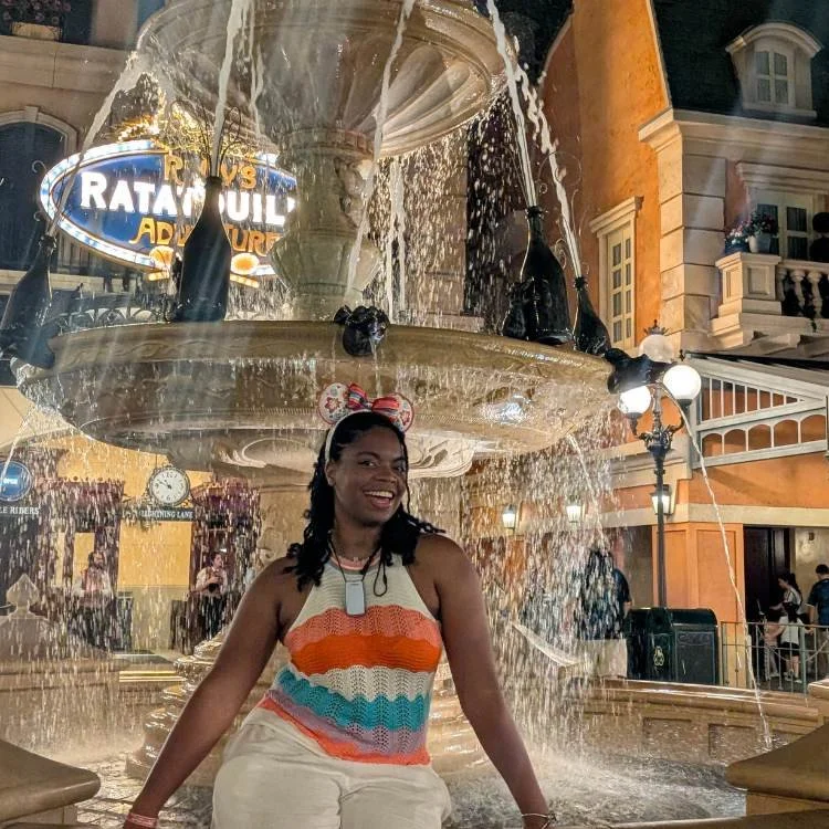 Black woman wearing Disney ears smiles in front of Epcot Remy's Ratatouille Adventure