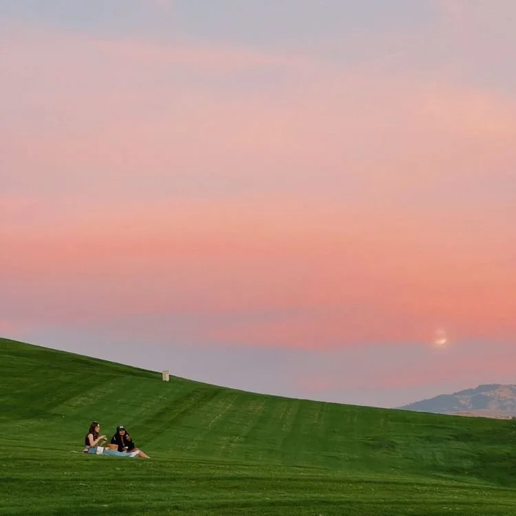 Two people sitting on a hill at sunset