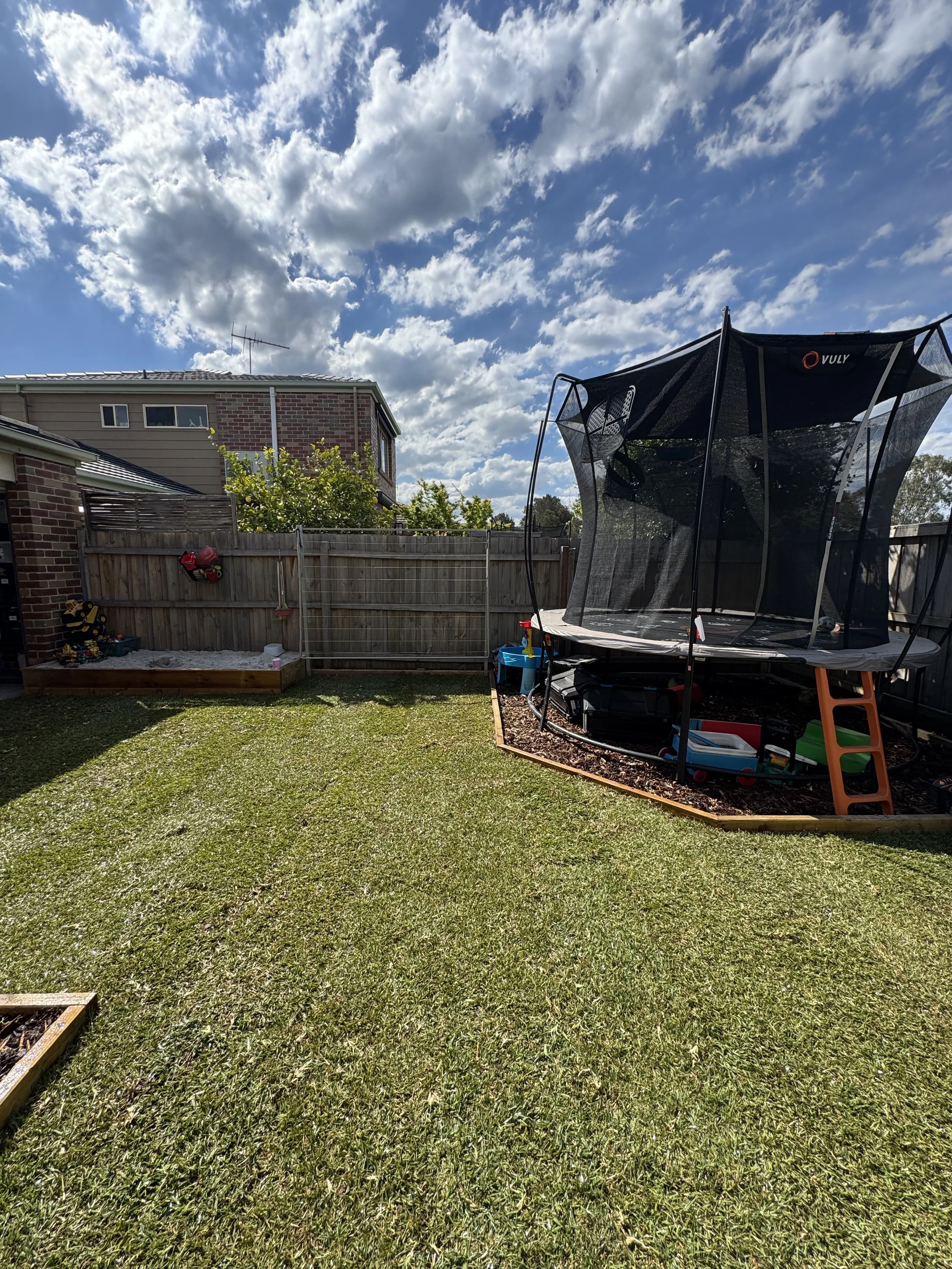 backyard with a trampoline, sandbox, and lawn under a partly cloudy sky