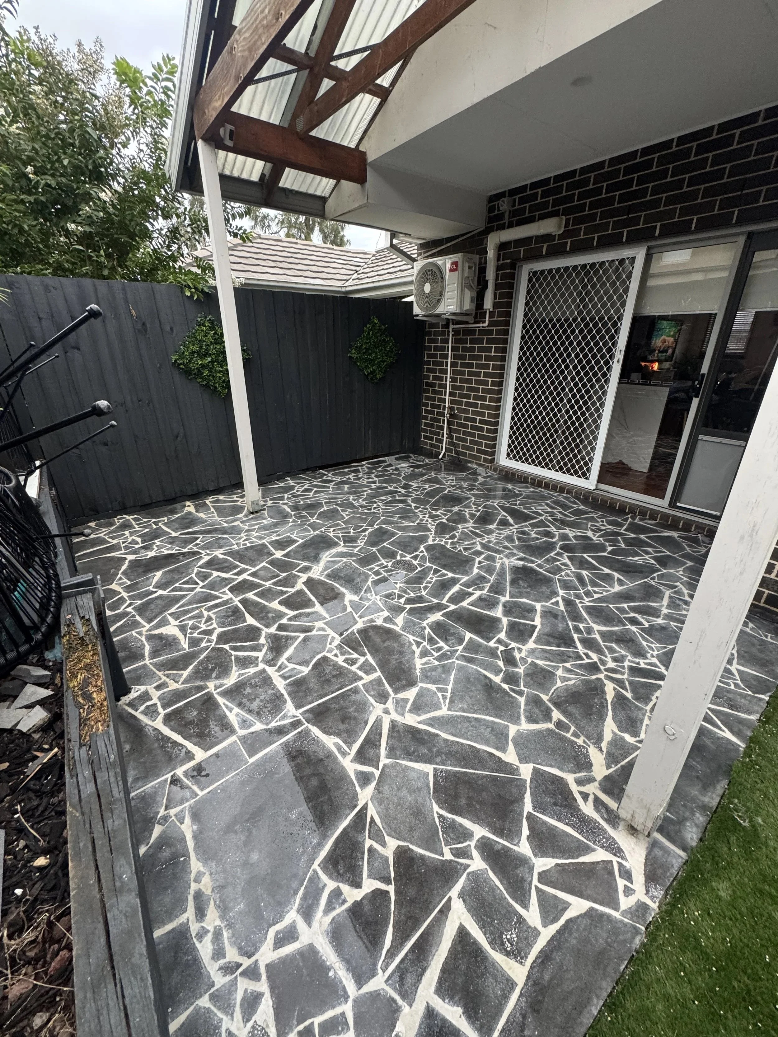 Back patio with bluestone crazy paving, black fence, and sliding glass door with security screen.