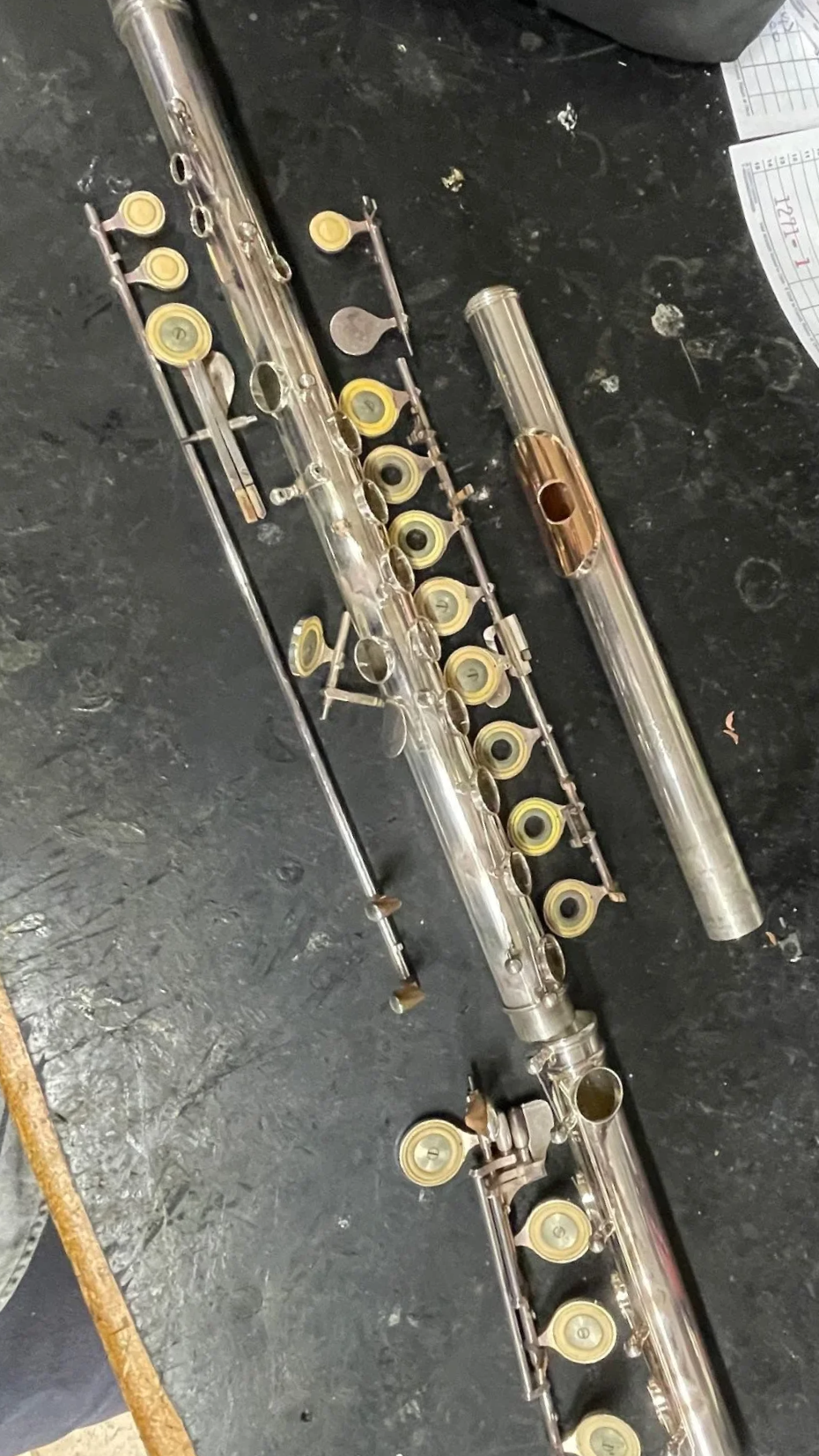 Disassembled silver flute with yellow pads on a black work surface.