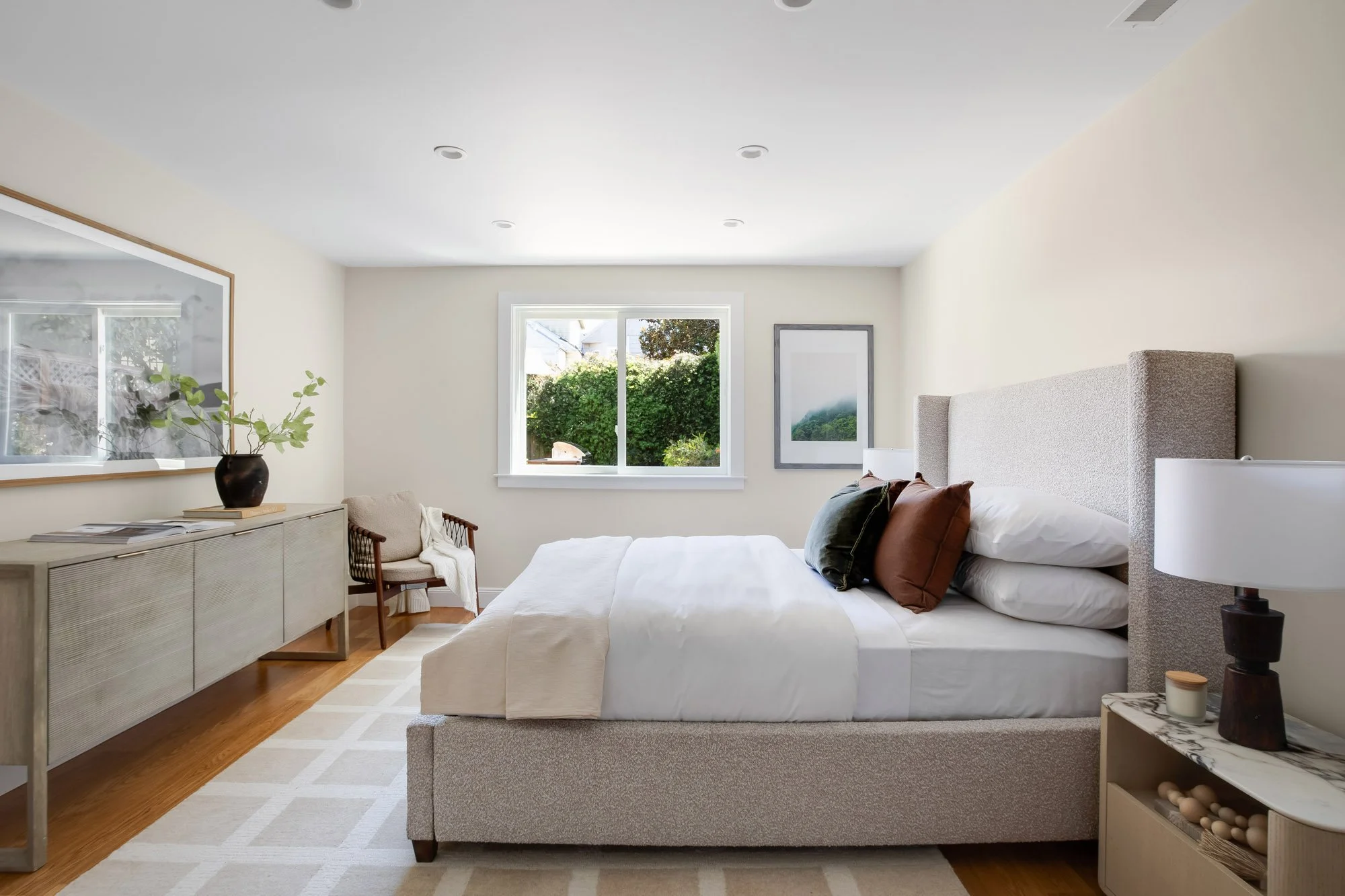 Ground level bedroom/guestroom/home office at 771 Elizabeth Street in Noe Valley with an upholstered wingback bed, garden-facing window, oversized mirror, marble-top nightstand, and warm hardwood floors.