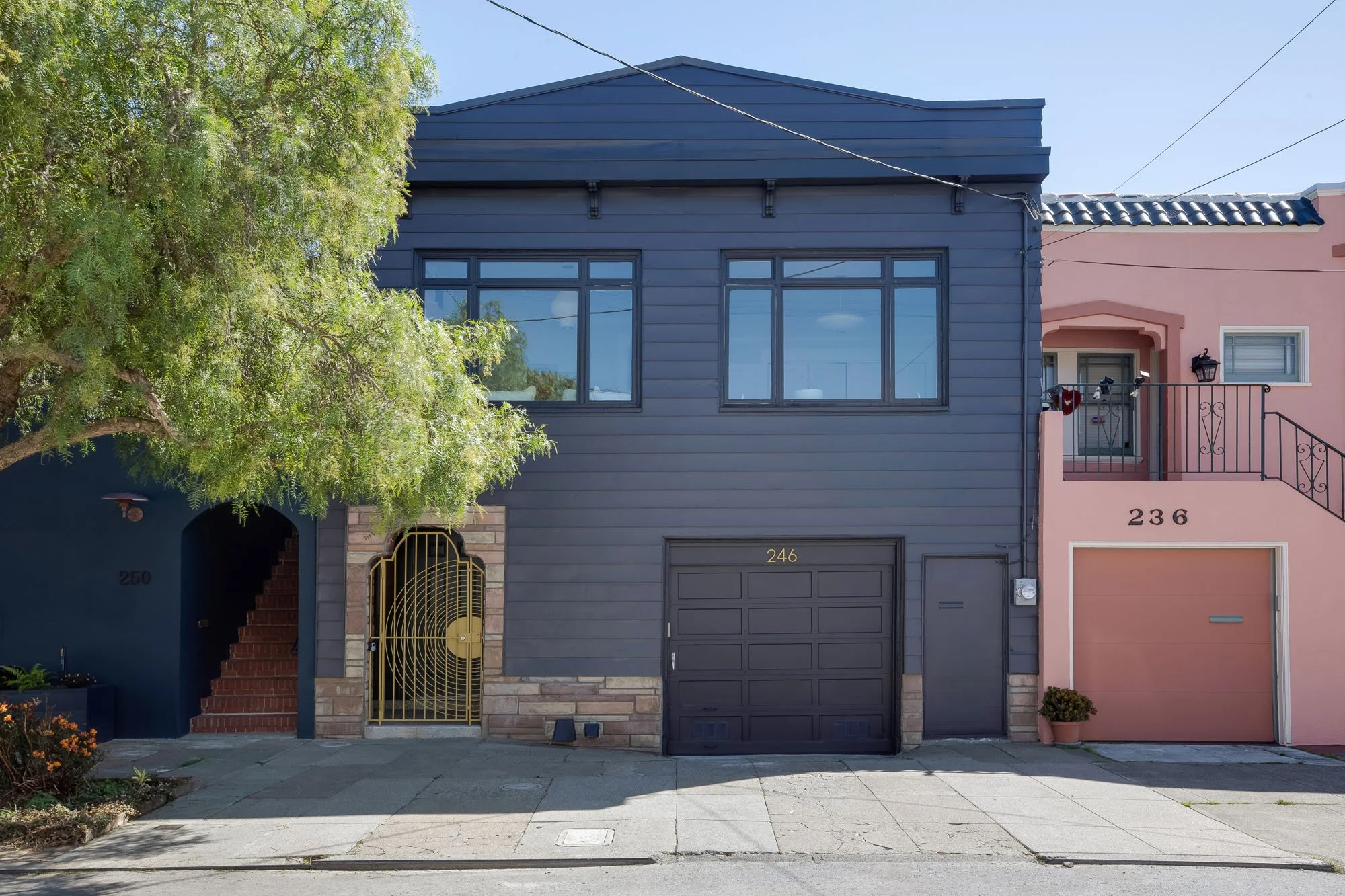 Front exterior of 246 Detroit in San Francisco, featuring a dark slate-gray facade, a decorative gold sunburst gate, and a two-car garage, flanked by a classic pink neighboring home.